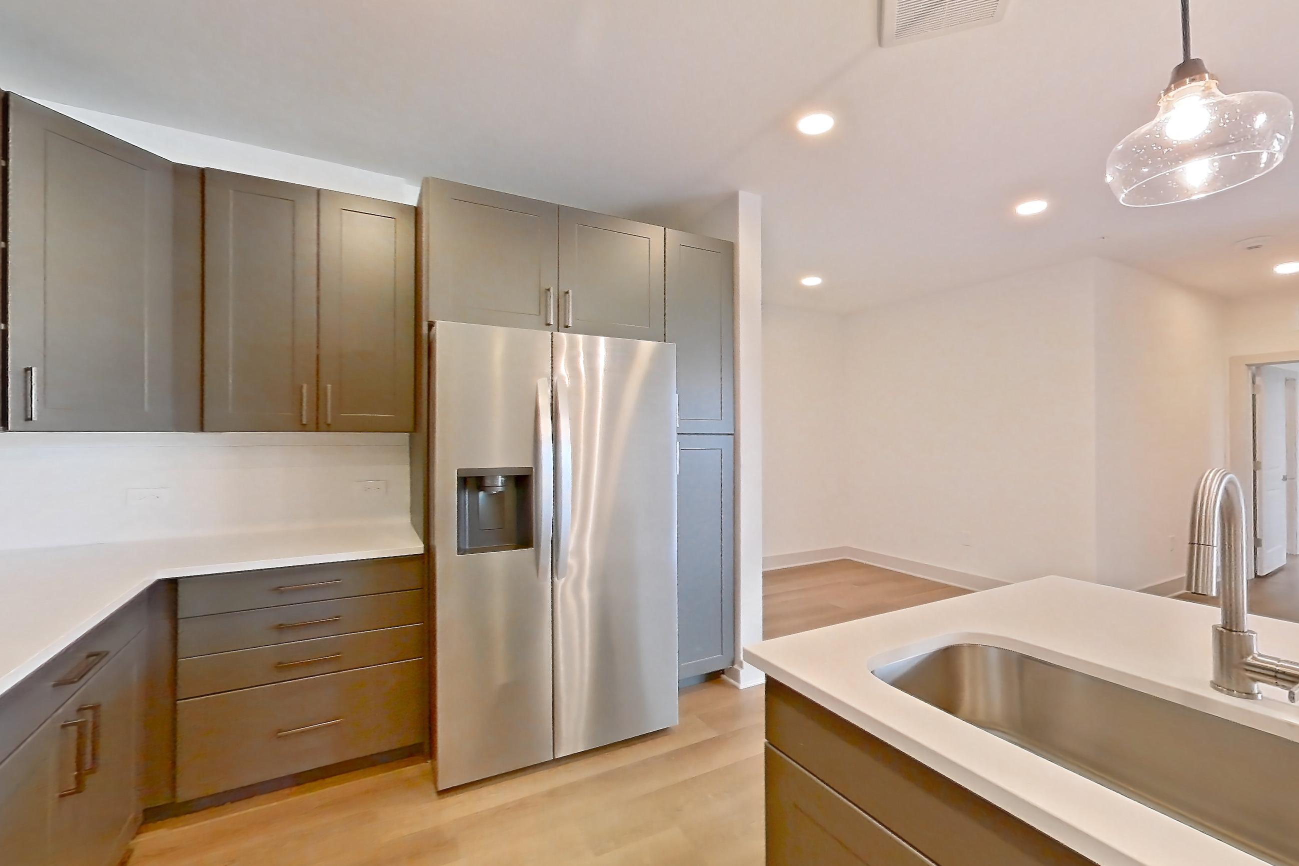 Kitchen with dishwasher, electric range, kitchen island, light countertops, light stone countertops, light wood-finish flooring, oven/range, refrigerator, stainless steel appliances, and water & ice dispenser, Apartment 2454 at Groves South Congress