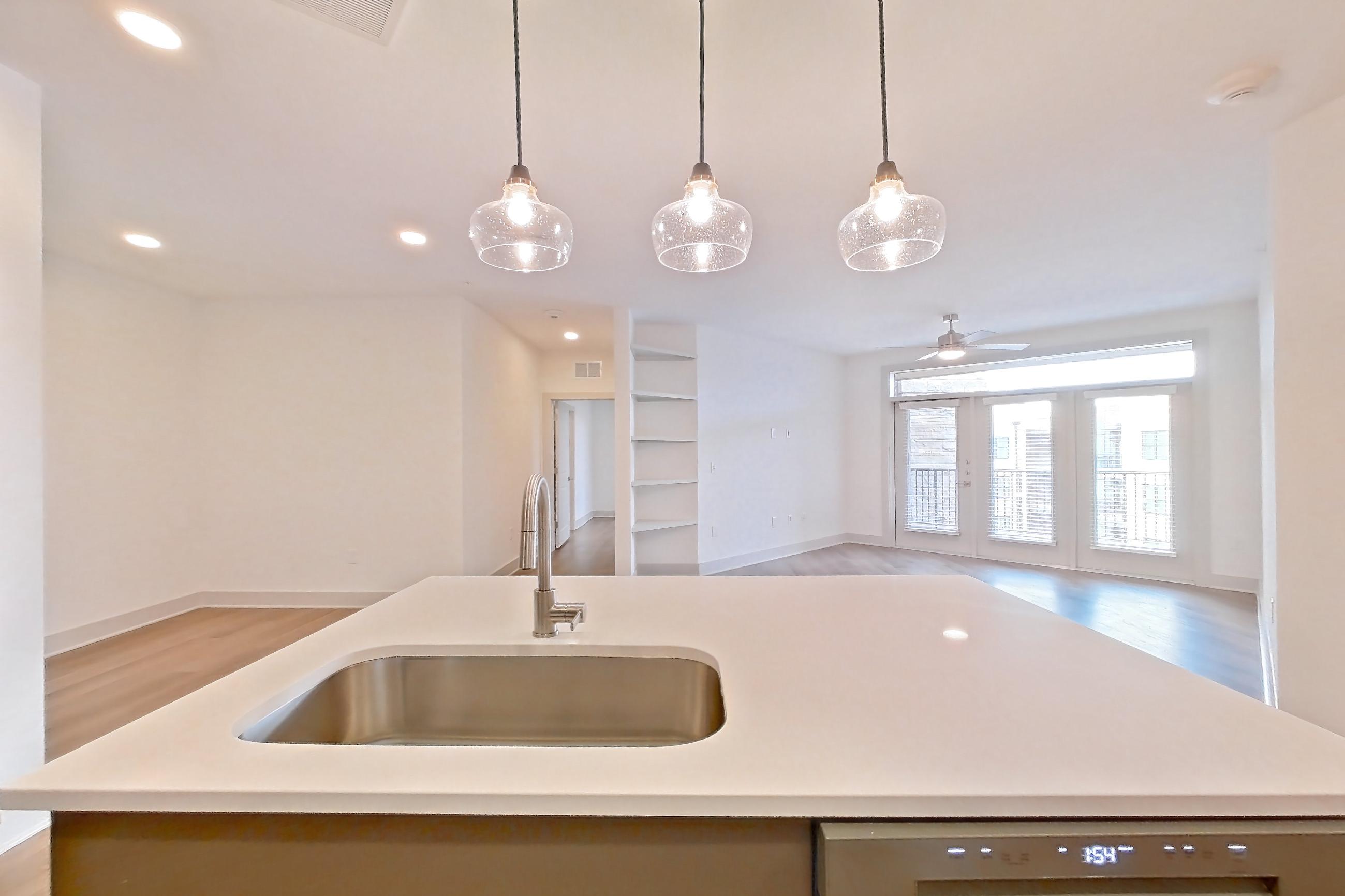 Kitchen with dishwasher, electric range, kitchen island, light countertops, light stone countertops, light wood-finish flooring, oven/range, refrigerator, stainless steel appliances, and water & ice dispenser, Apartment 2454 at Groves South Congress