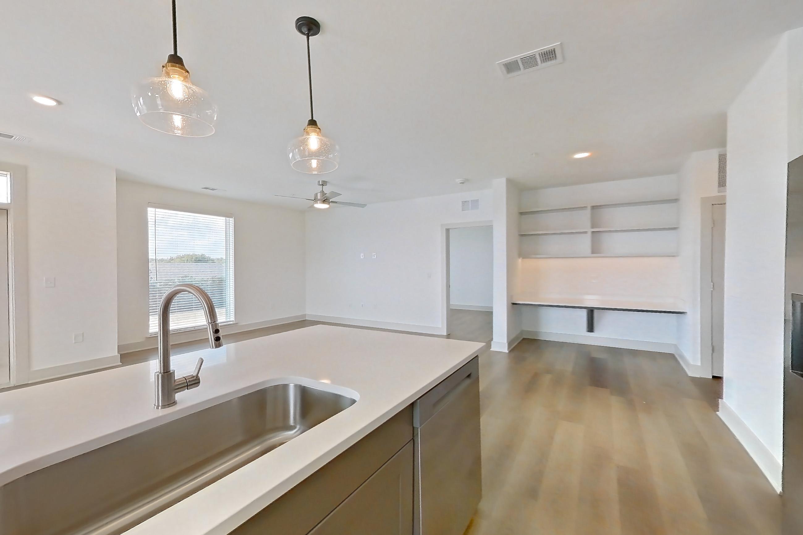 Kitchen with dishwasher, electric range, kitchen island, light countertops, light stone countertops, light wood-finish flooring, oven/range, and stainless steel appliances, Apartment 2201 at Groves South Congress