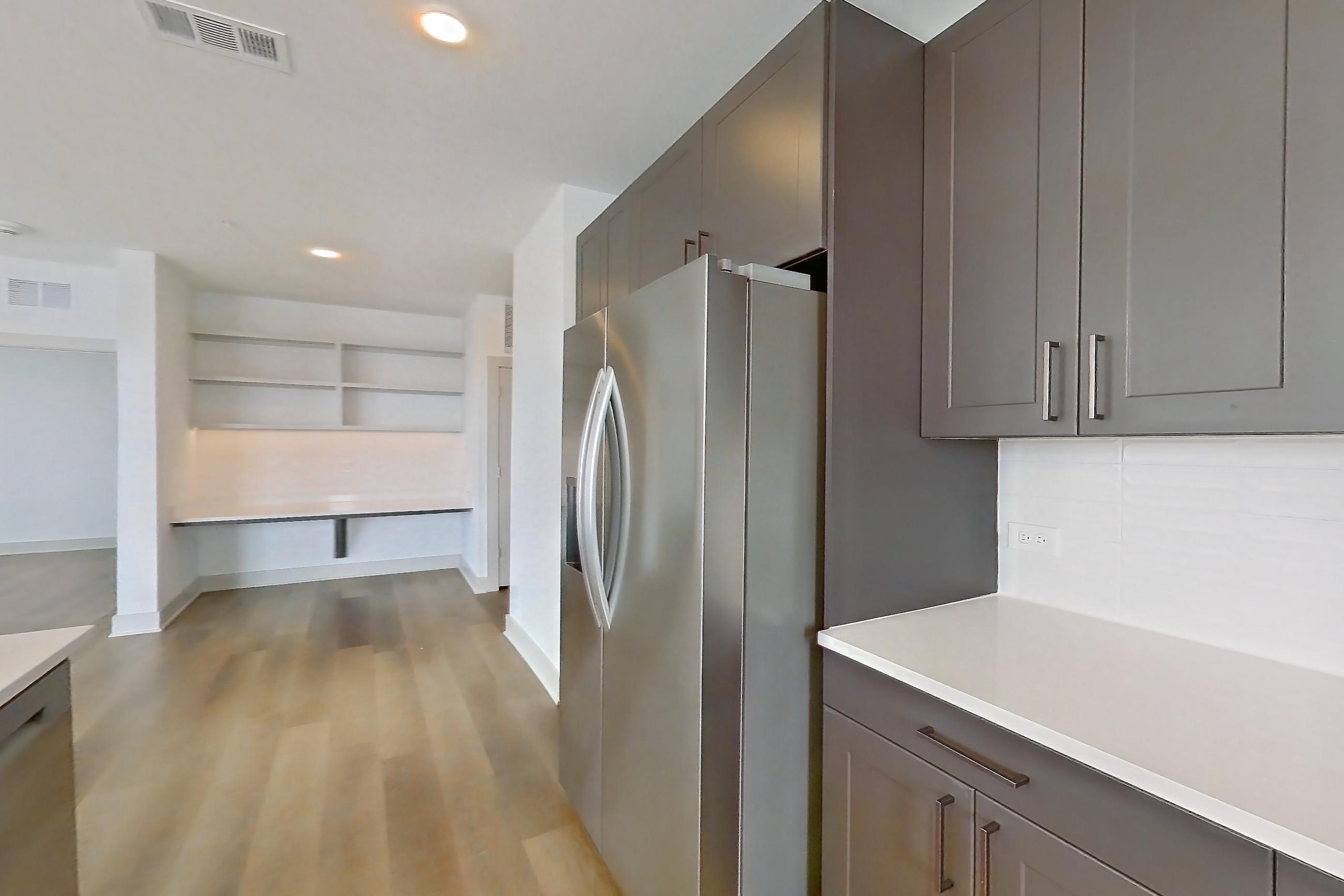 Kitchen with dishwasher, electric range, kitchen island, light countertops, light stone countertops, light wood-finish flooring, oven/range, and stainless steel appliances, Apartment 2201 at Groves South Congress
