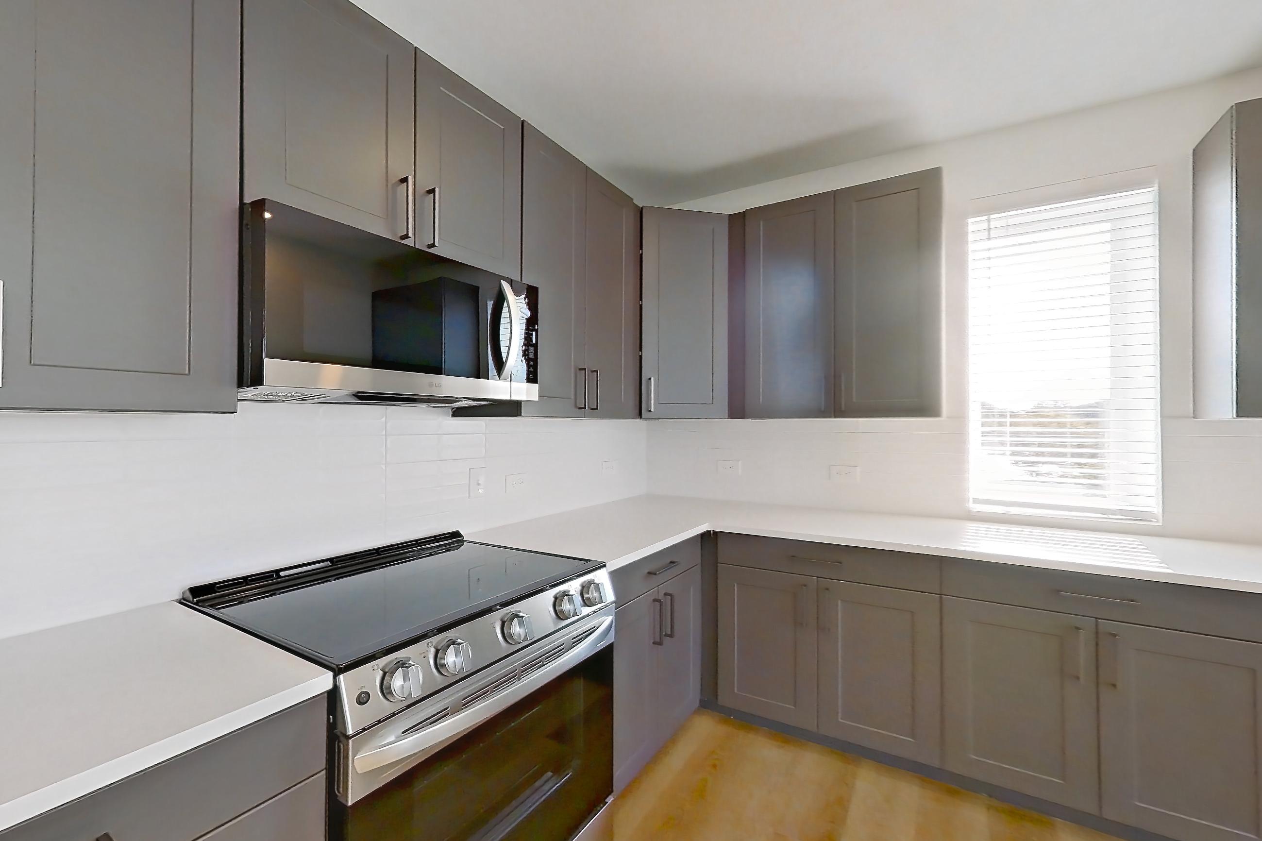 Kitchen with dishwasher, electric range, kitchen island, light countertops, light stone countertops, light wood-finish flooring, oven/range, and stainless steel appliances, Apartment 2201 at Groves South Congress