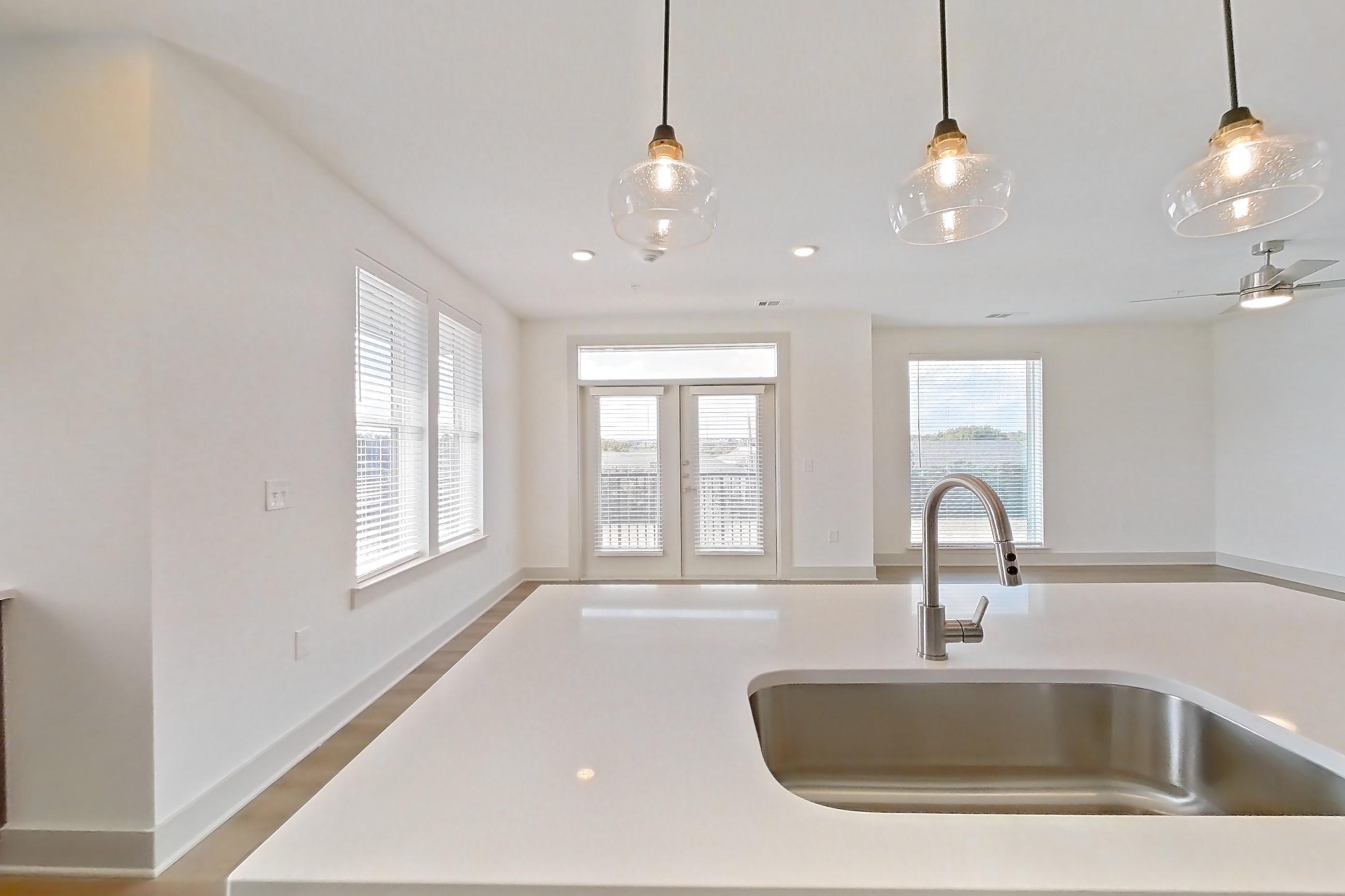 Kitchen with dishwasher, electric range, kitchen island, light countertops, light stone countertops, light wood-finish flooring, oven/range, and stainless steel appliances, Apartment 2201 at Groves South Congress