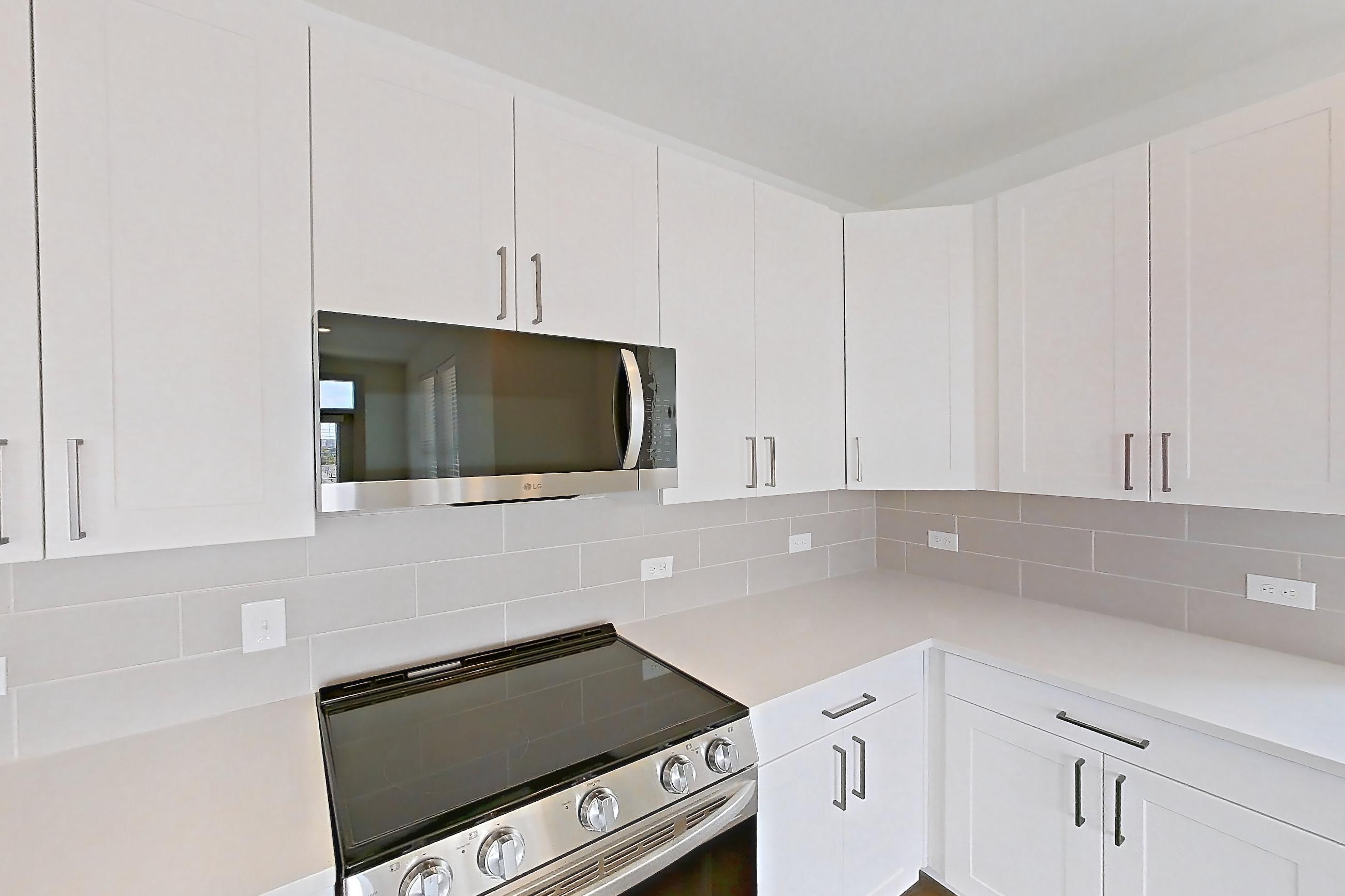 Kitchen with dark wood-finish flooring, electric range, light countertops, light stone countertops, microwave, oven/range, refrigerator, and stainless steel appliances, Apartment 2301 at Groves South Congress