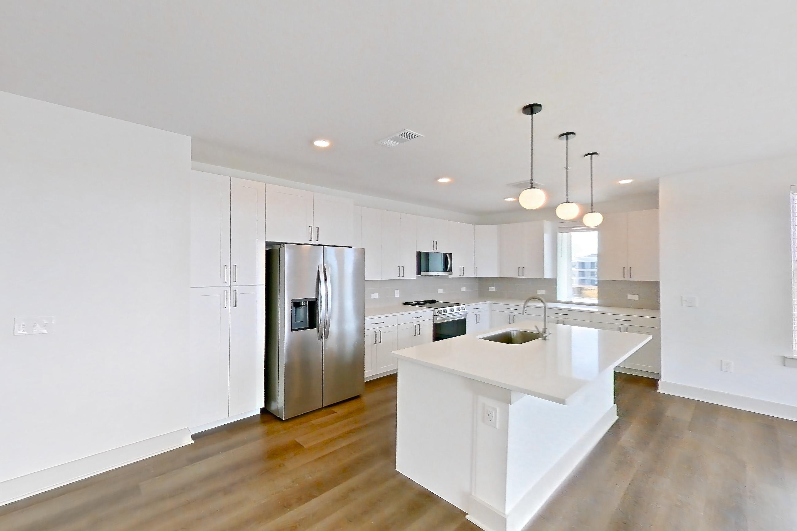 Living room with dark wood-finish flooring, electric range, kitchen island, light countertops, oven/range, refrigerator, stainless steel appliances, and water & ice dispenser, Apartment 2301 at Groves South Congress