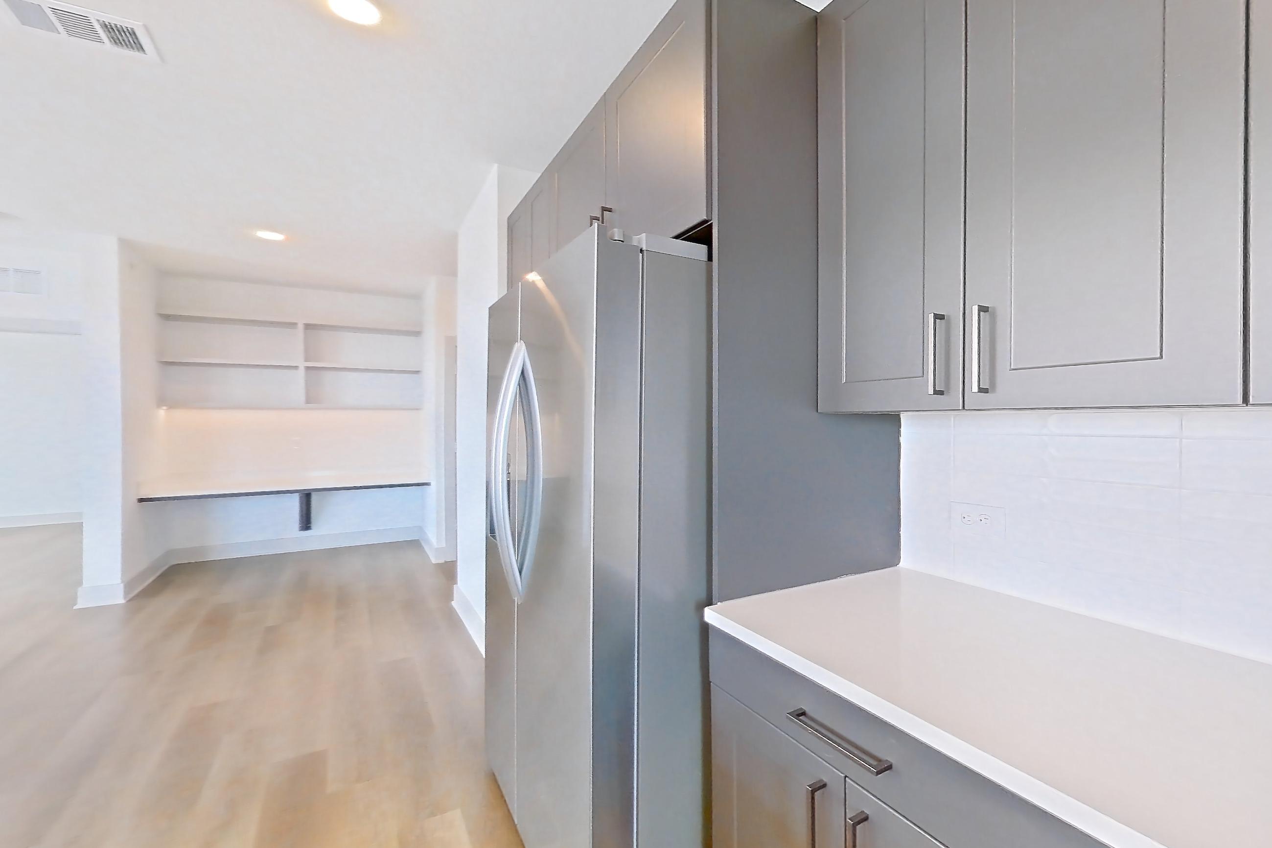 Kitchen with electric range, kitchen island, light countertops, light stone countertops, light wood-finish flooring, oven/range, refrigerator, and stainless steel appliances, Apartment 2401 at Groves South Congress