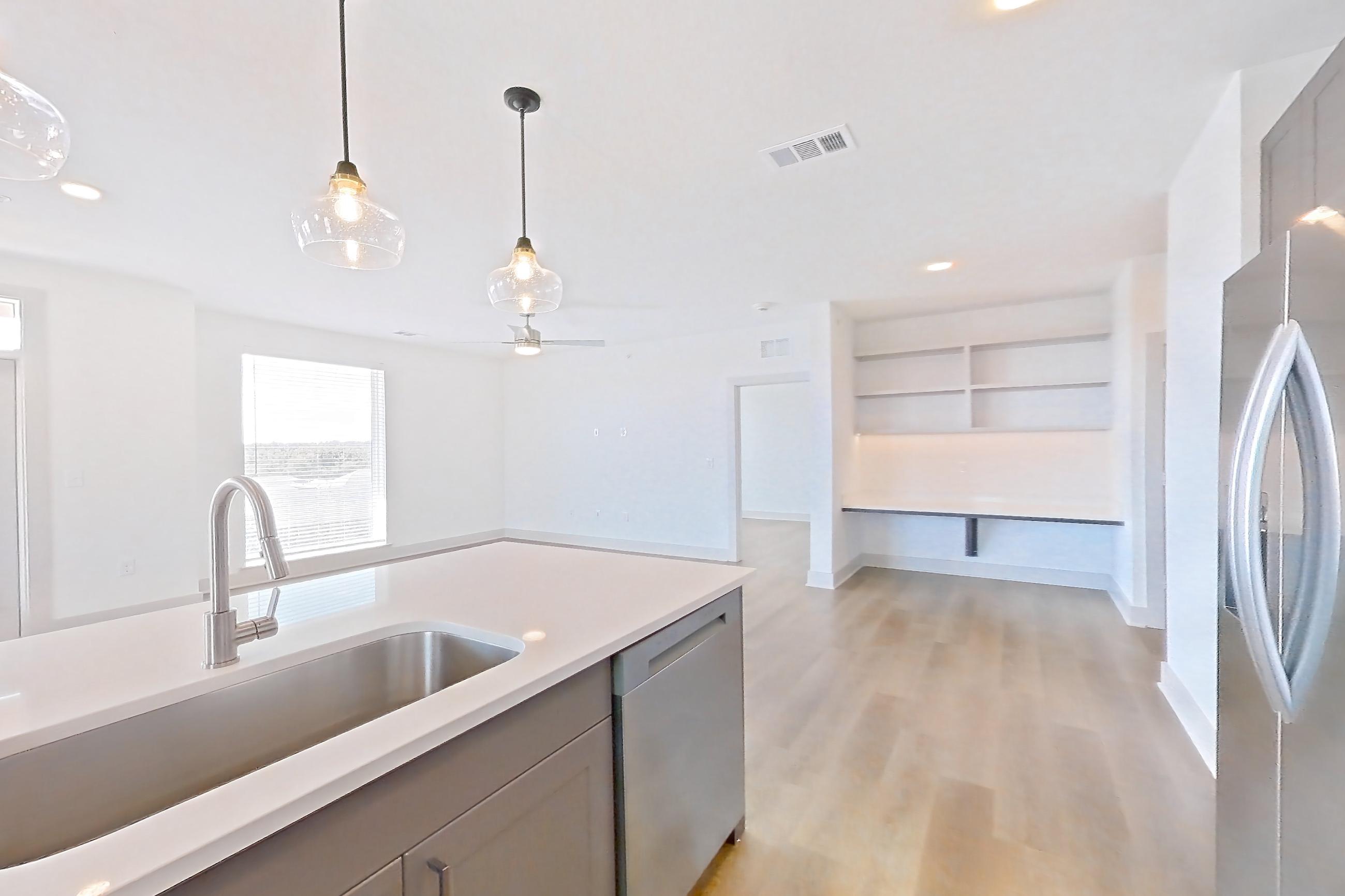 Kitchen with electric range, kitchen island, light countertops, light stone countertops, light wood-finish flooring, oven/range, refrigerator, and stainless steel appliances, Apartment 2401 at Groves South Congress