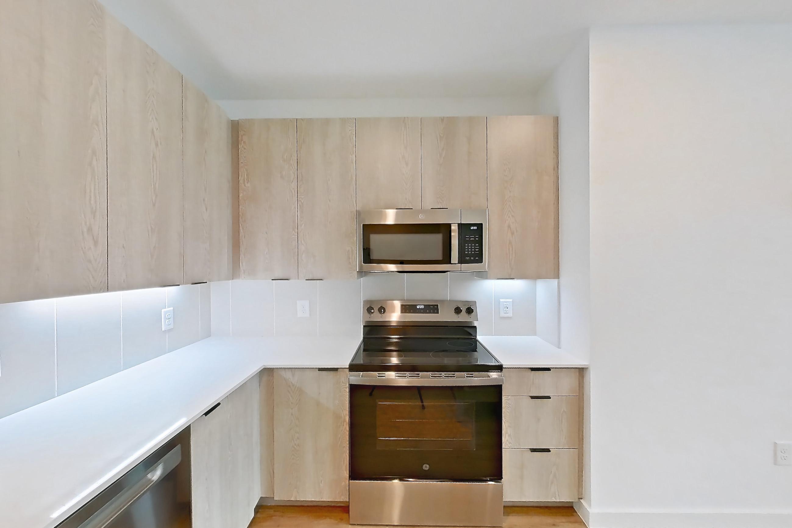 Kitchen with dishwasher, electric range, light countertops, light stone countertops, light wood-finish flooring, microwave, oven/range, and stainless steel appliances, Apartment 1109 at Caroline Anclote Harbor