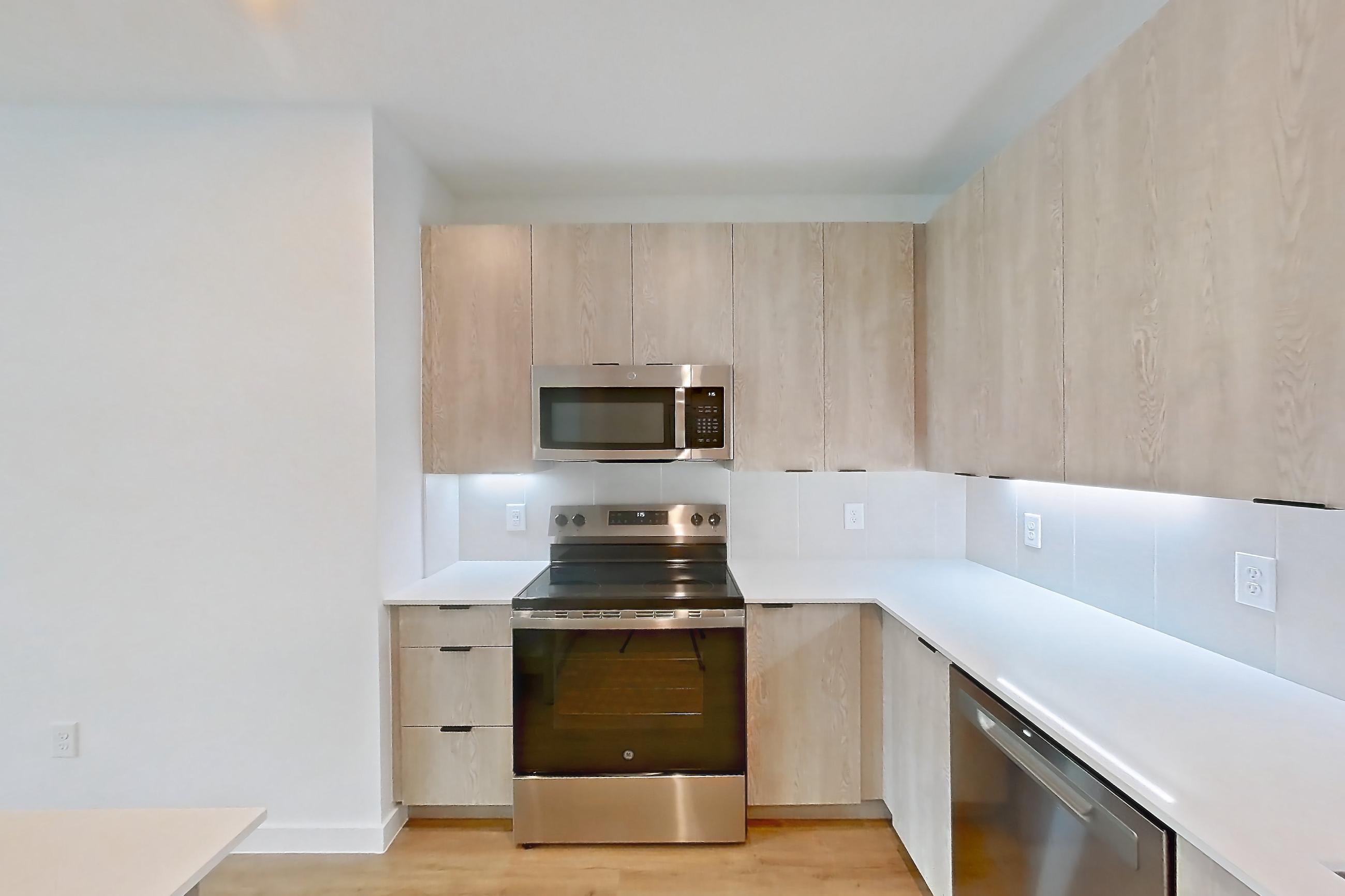 Kitchen with dishwasher, electric range, light countertops, light wood-finish flooring, microwave, oven/range, and stainless steel appliances, Apartment 1204 at Caroline Anclote Harbor