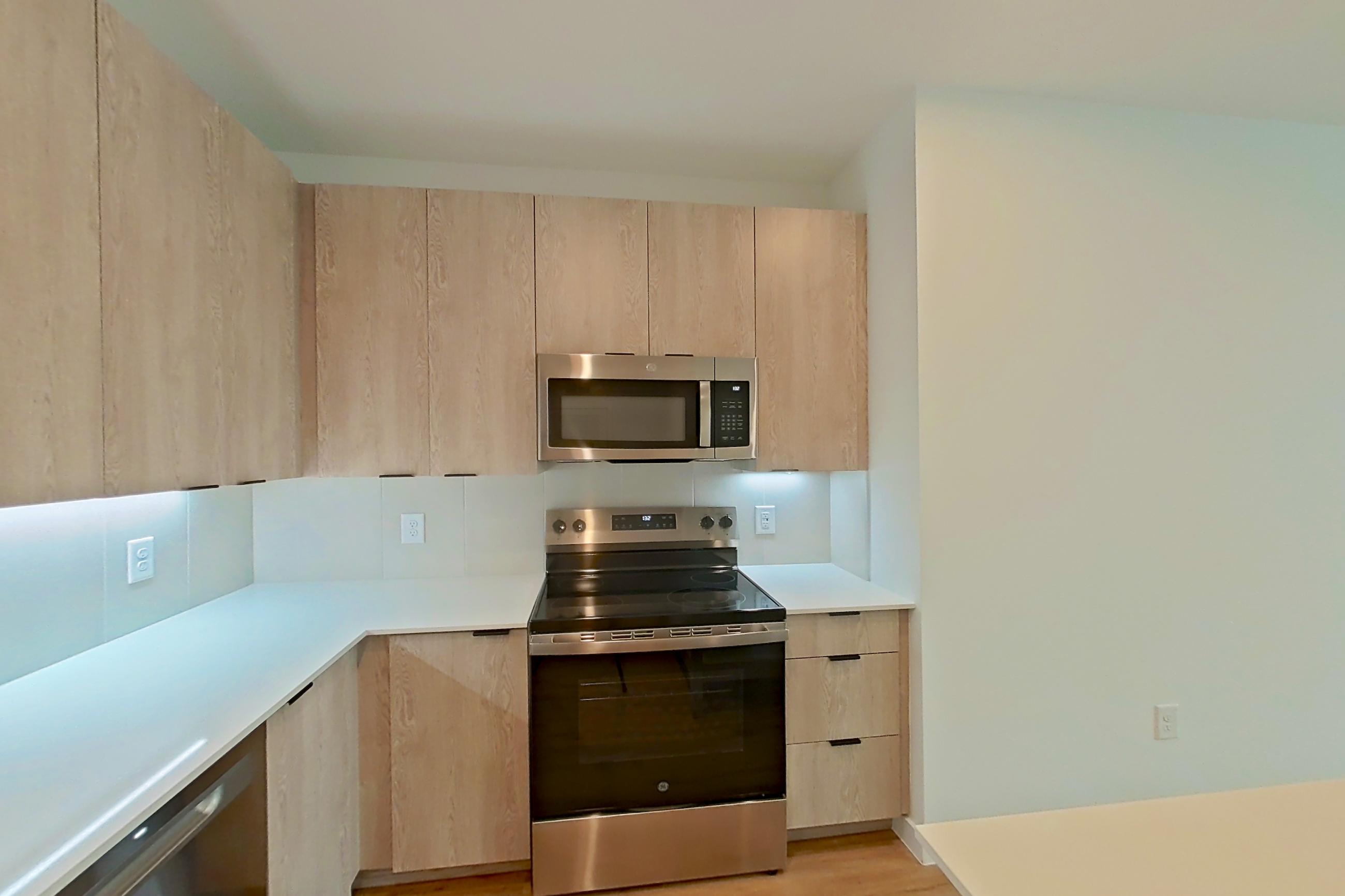 Kitchen with dishwasher, electric range, light countertops, light stone countertops, light wood-finish flooring, microwave, oven/range, and stainless steel appliances, Apartment 1209 at Caroline Anclote Harbor