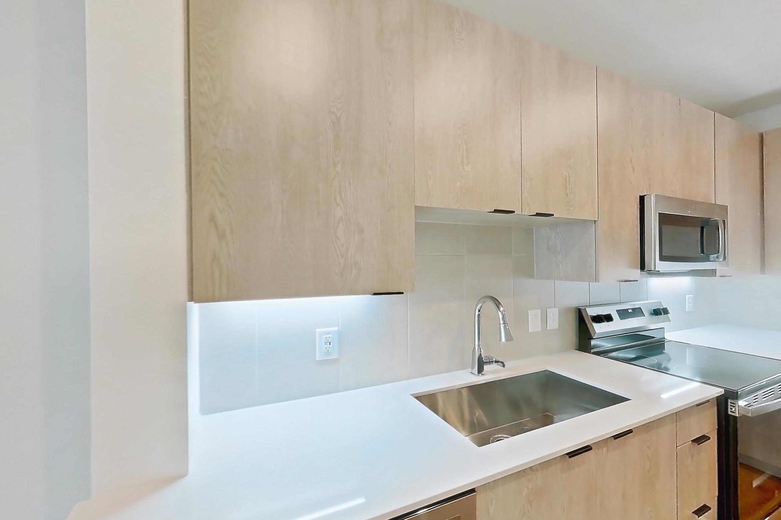 Kitchen with dishwasher, electric range, light countertops, light stone countertops, light wood-finish flooring, oven/range, refrigerator, and stainless steel appliances, Apartment 1210 at Caroline Anclote Harbor