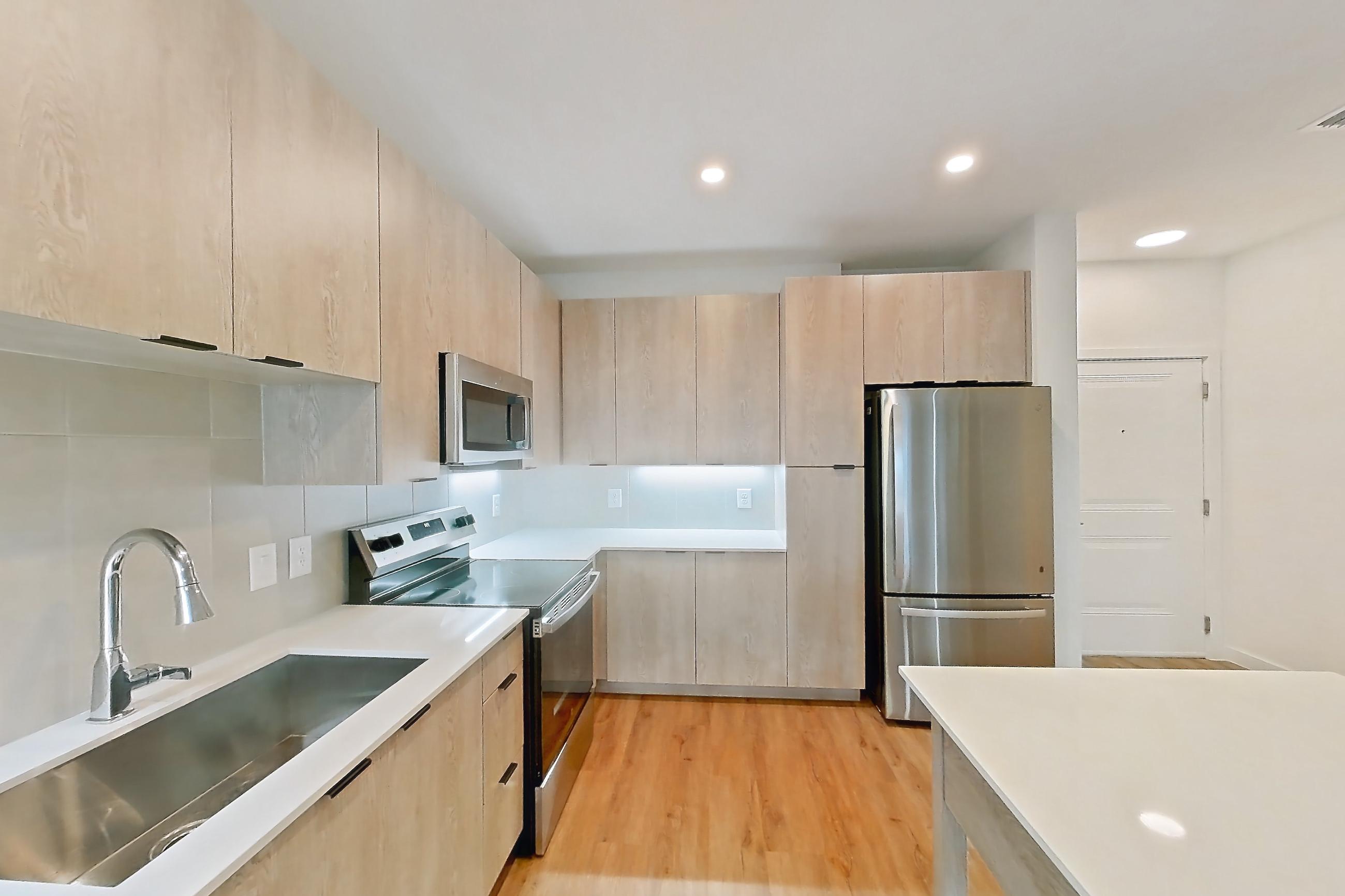 Kitchen with dishwasher, electric range, light countertops, light stone countertops, light wood-finish flooring, oven/range, refrigerator, and stainless steel appliances, Apartment 1210 at Caroline Anclote Harbor