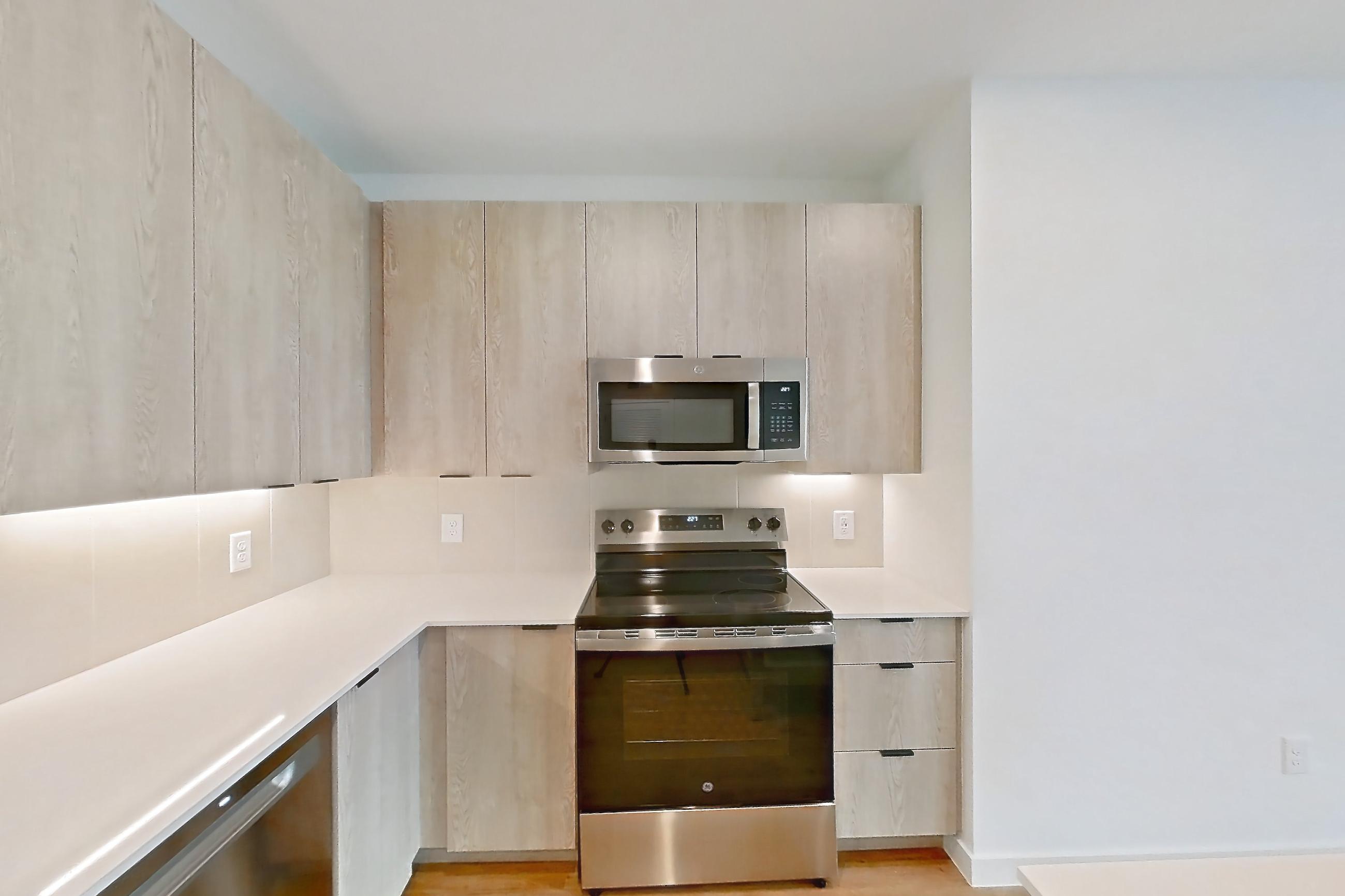 Kitchen with dishwasher, electric range, light countertops, light wood-finish flooring, microwave, oven/range, and stainless steel appliances, Apartment 1213 at Caroline Anclote Harbor