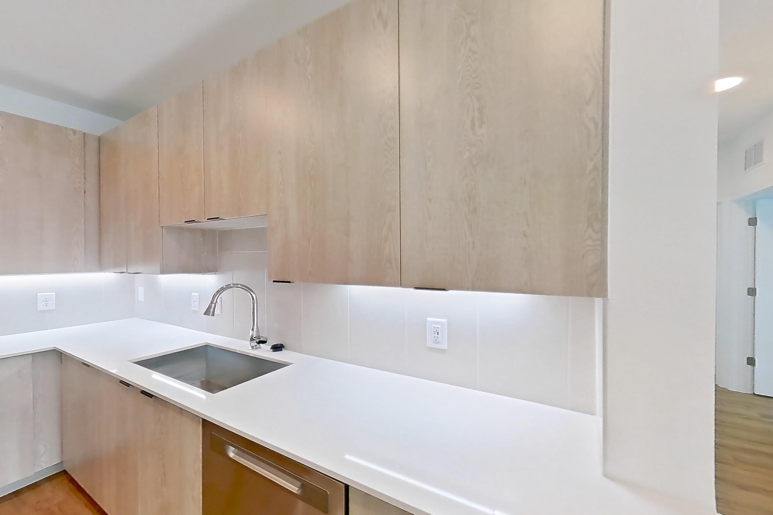 Kitchen with dishwasher, electric range, light countertops, light stone countertops, light wood-finish flooring, microwave, oven/range, refrigerator, and stainless steel appliances, Apartment 1215 at Caroline Anclote Harbor