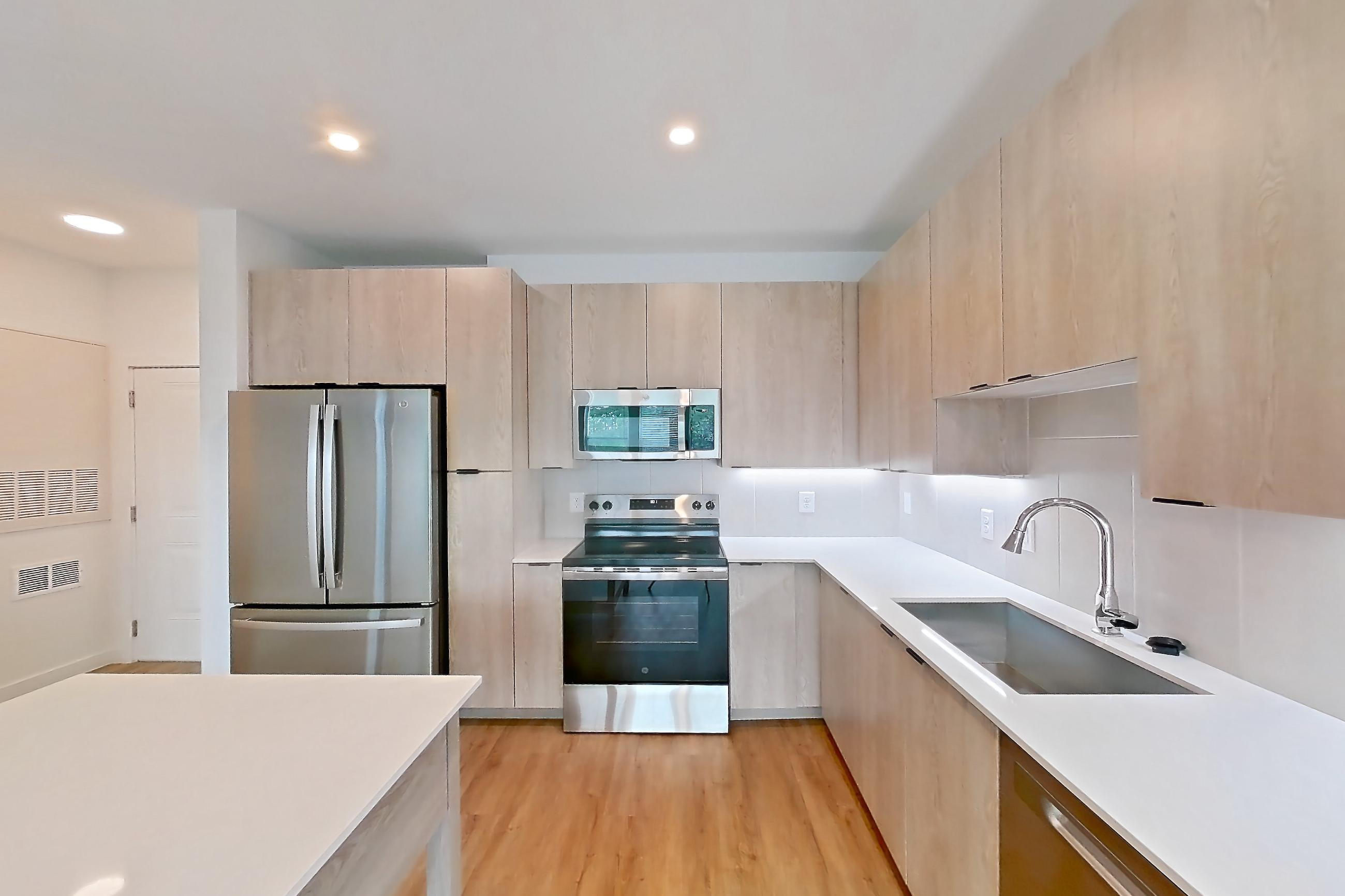Kitchen with dishwasher, electric range, light countertops, light stone countertops, light wood-finish flooring, microwave, oven/range, refrigerator, and stainless steel appliances, Apartment 1215 at Caroline Anclote Harbor