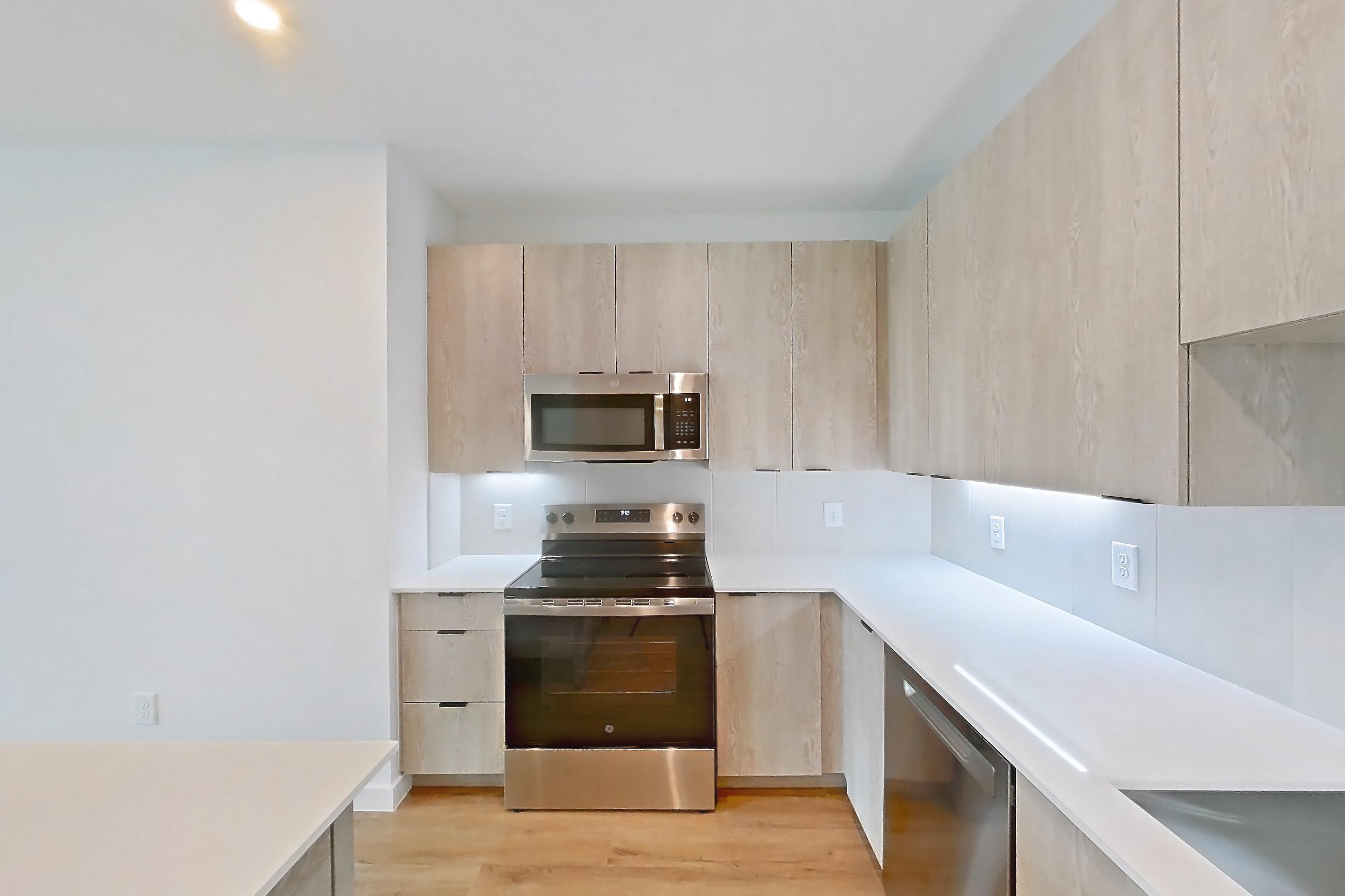 Kitchen with dishwasher, electric range, light stone countertops, light wood-finish flooring, microwave, oven/range, and stainless steel appliances, Apartment 1219 at Caroline Anclote Harbor