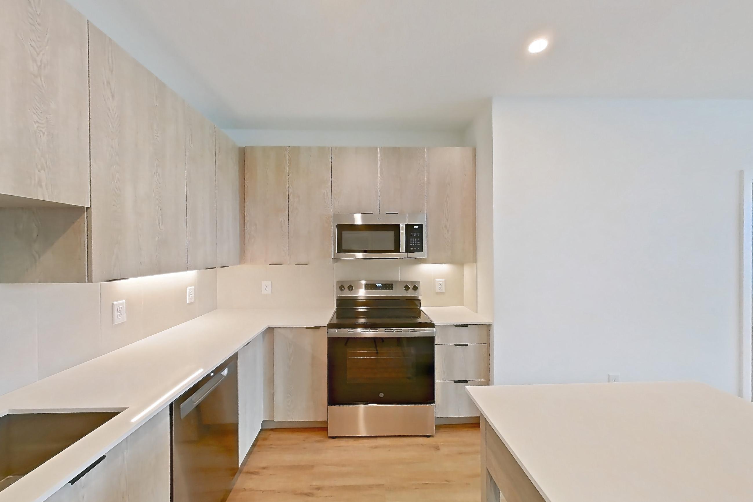 Kitchen with dishwasher, electric range, light countertops, light wood-finish flooring, microwave, oven/range, and stainless steel appliances, Apartment 1301 at Caroline Anclote Harbor