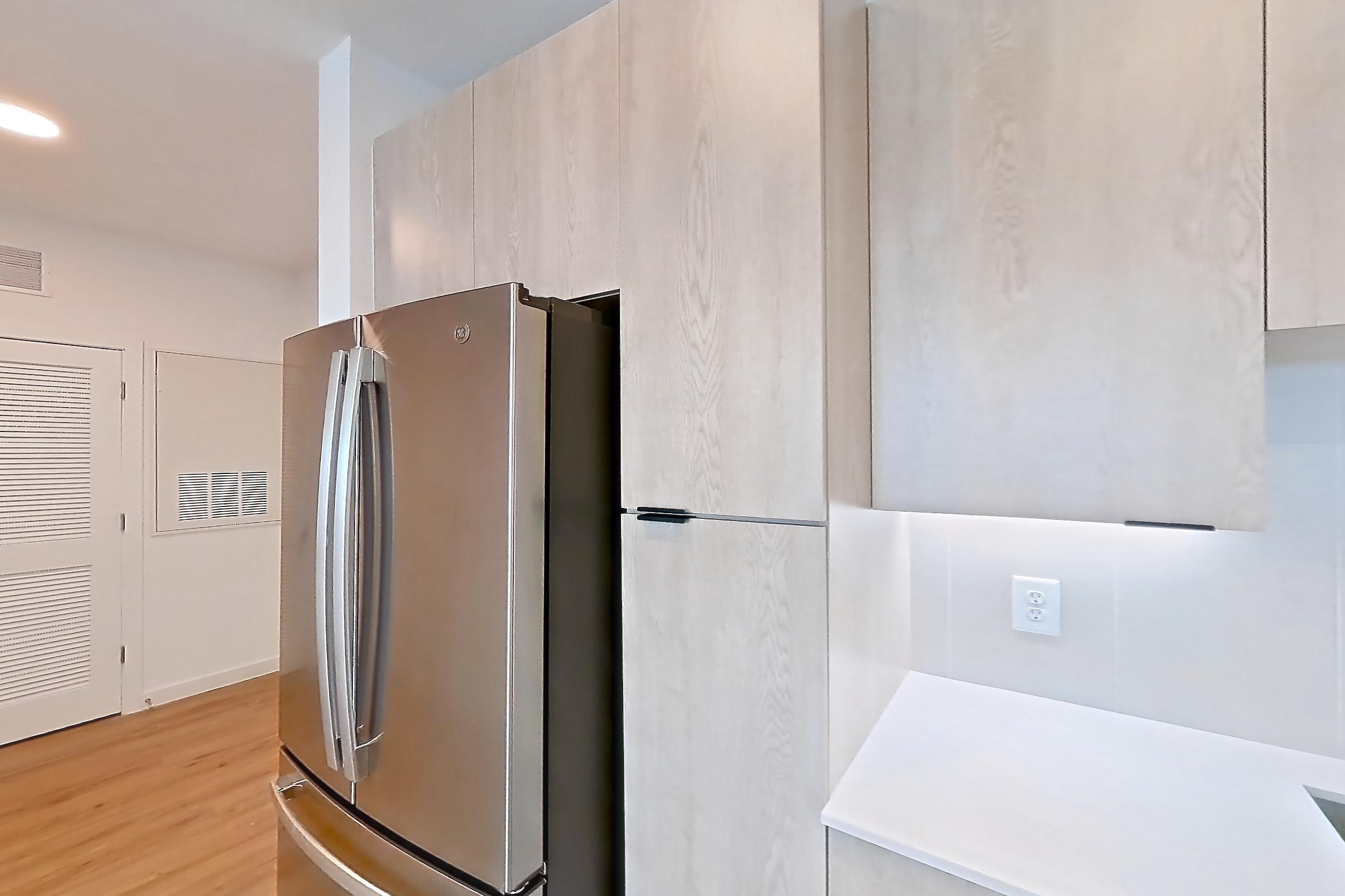 Kitchen with dishwasher, electric range, light countertops, light stone countertops, light wood-finish flooring, microwave, oven/range, refrigerator, and stainless steel appliances, Apartment 1306 at Caroline Anclote Harbor