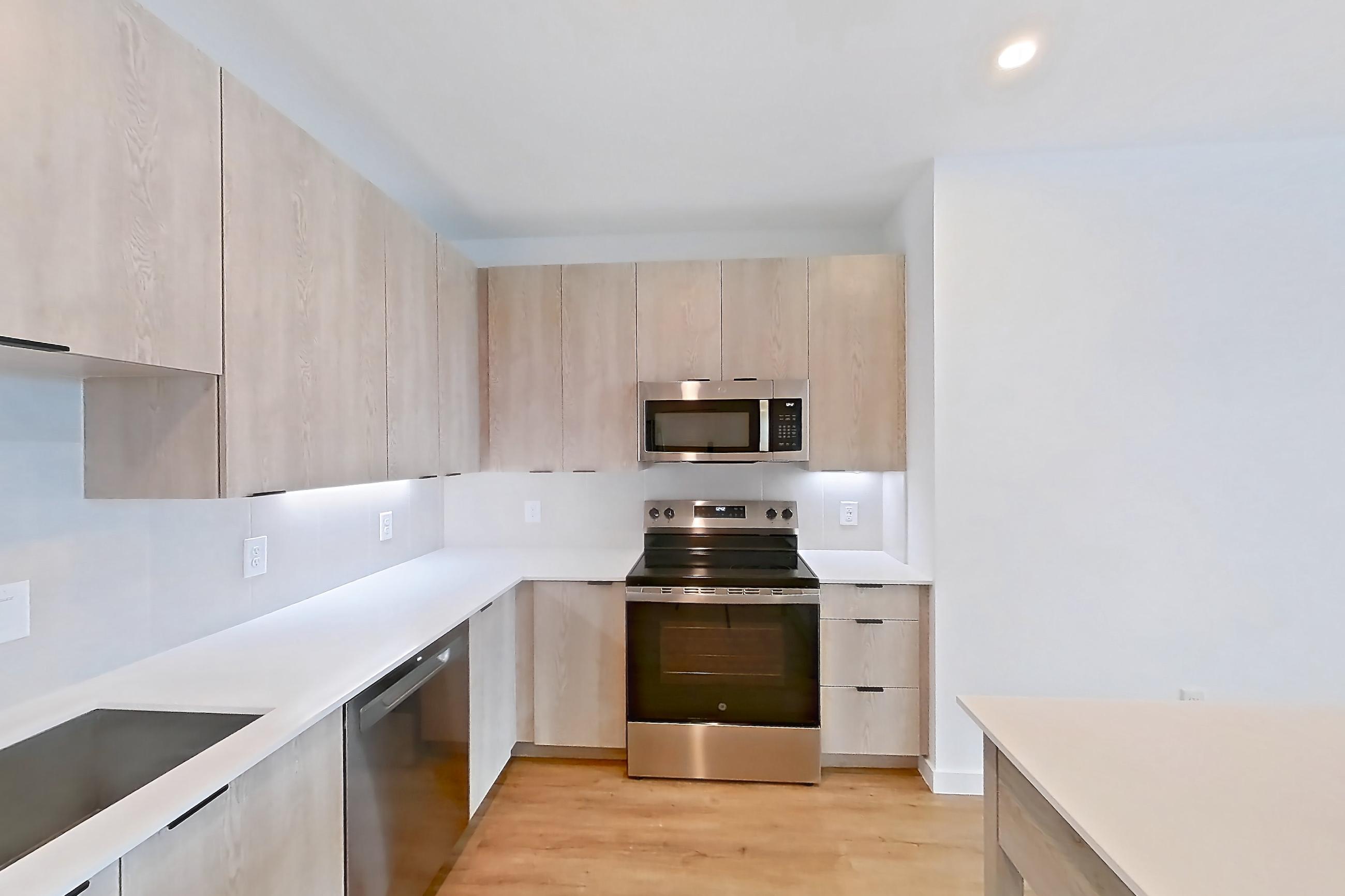 Kitchen with dishwasher, electric range, light countertops, light stone countertops, light wood-finish flooring, microwave, oven/range, refrigerator, and stainless steel appliances, Apartment 1306 at Caroline Anclote Harbor