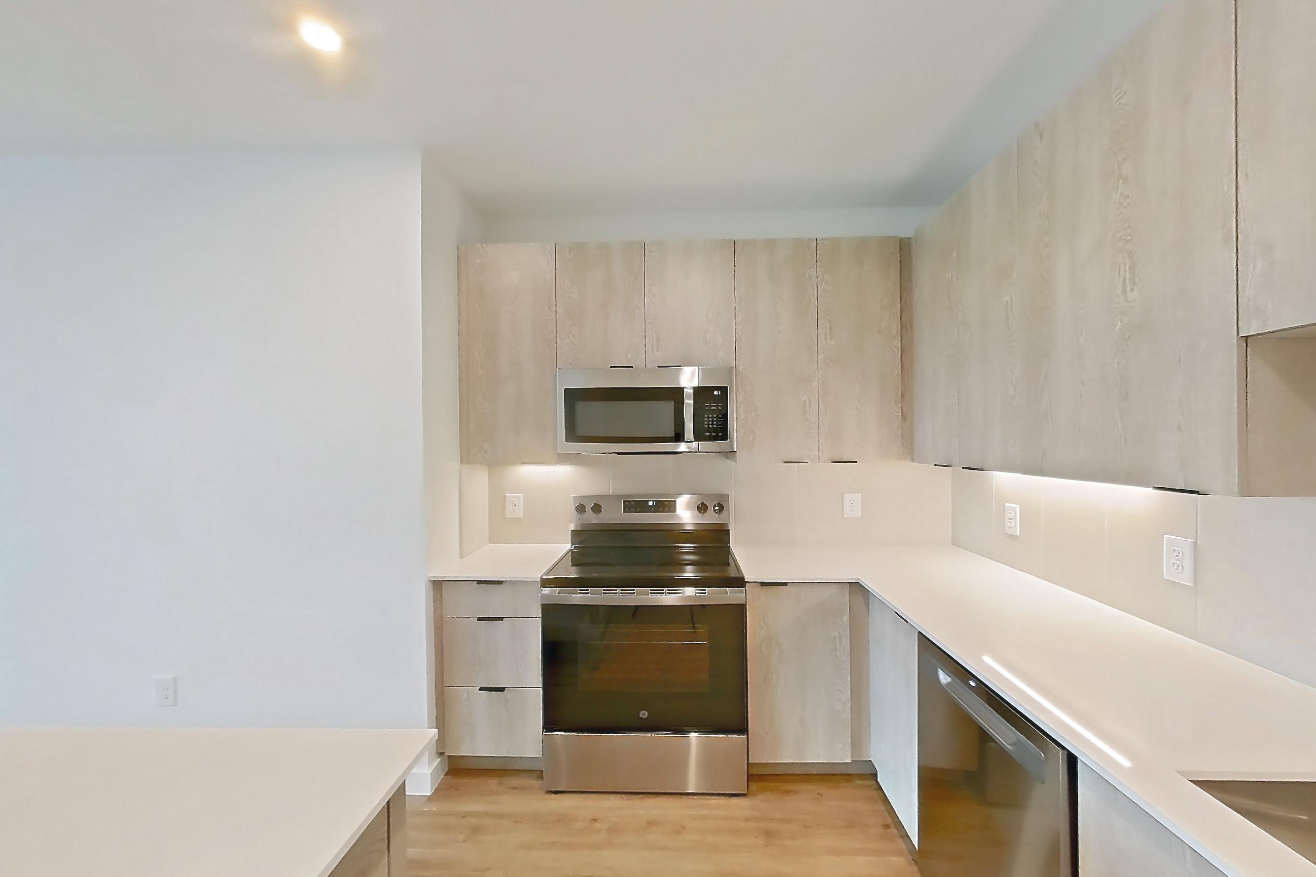 Kitchen with dishwasher, electric range, light countertops, light wood-finish flooring, microwave, oven/range, and stainless steel appliances, Apartment 1311 at Caroline Anclote Harbor