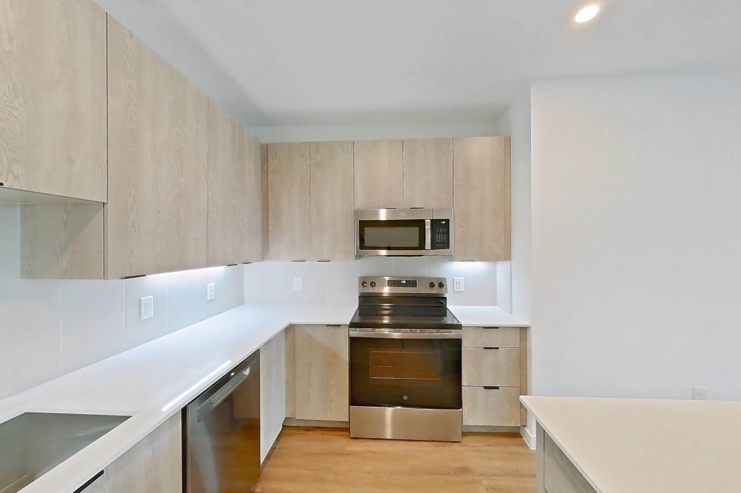 Kitchen with dishwasher, electric range, light countertops, light wood-finish flooring, microwave, oven/range, and stainless steel appliances, Apartment 1313 at Caroline Anclote Harbor