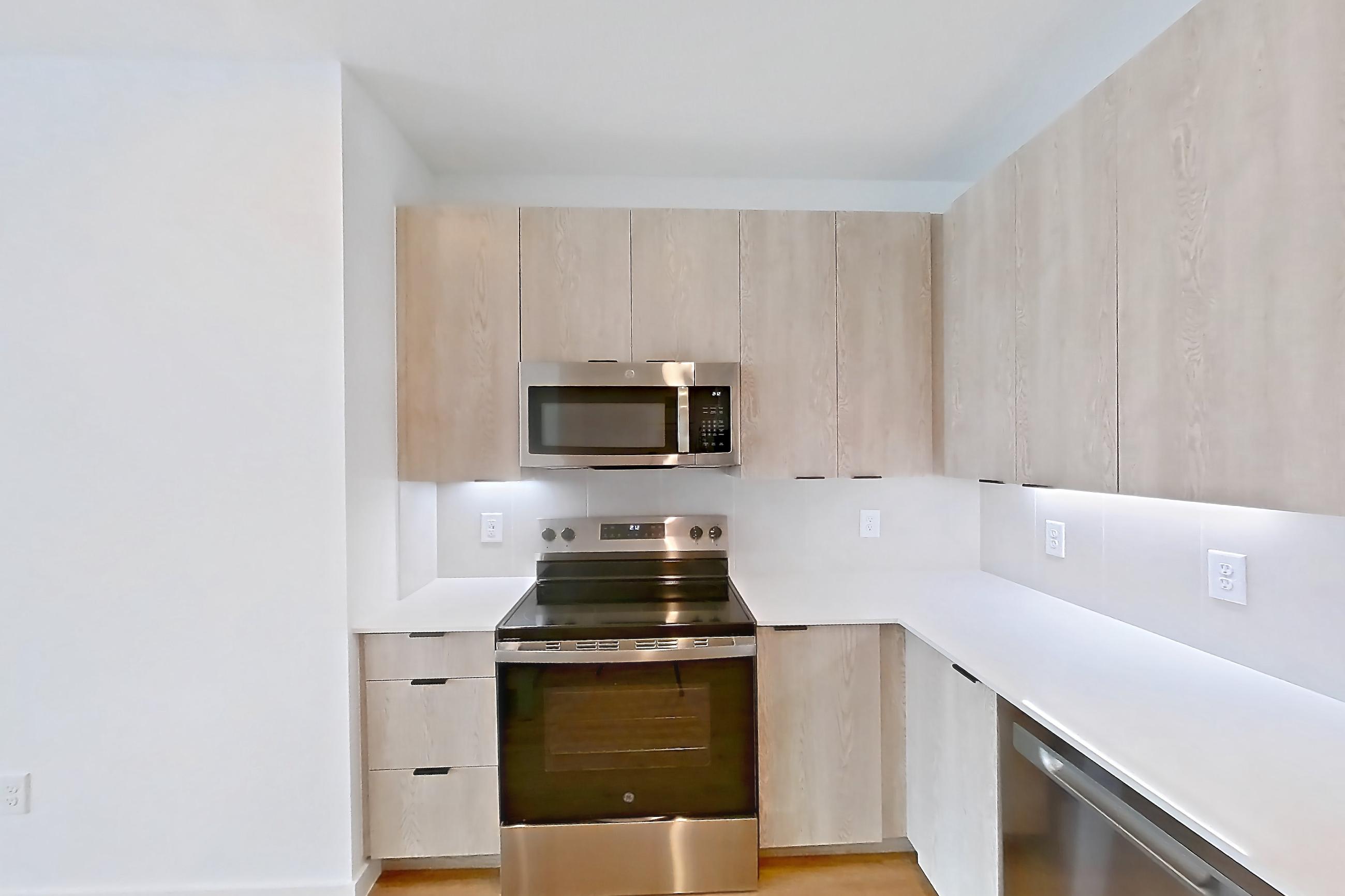 Kitchen with dishwasher, electric range, light countertops, light wood-finish flooring, microwave, oven/range, and stainless steel appliances, Apartment 1404 at Caroline Anclote Harbor