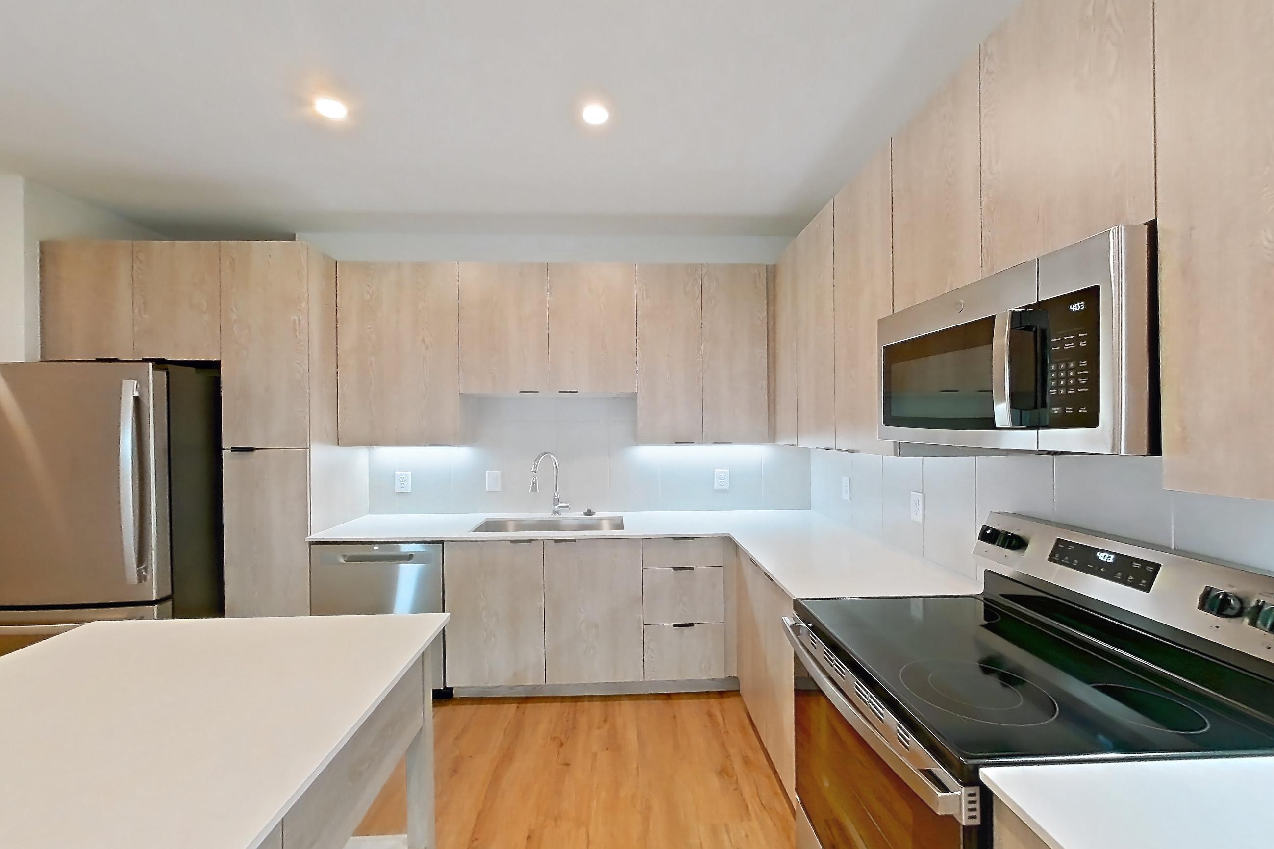 Kitchen with dishwasher, electric range, light countertops, light wood-finish flooring, oven/range, refrigerator, and stainless steel appliances, Apartment 1405 at Caroline Anclote Harbor