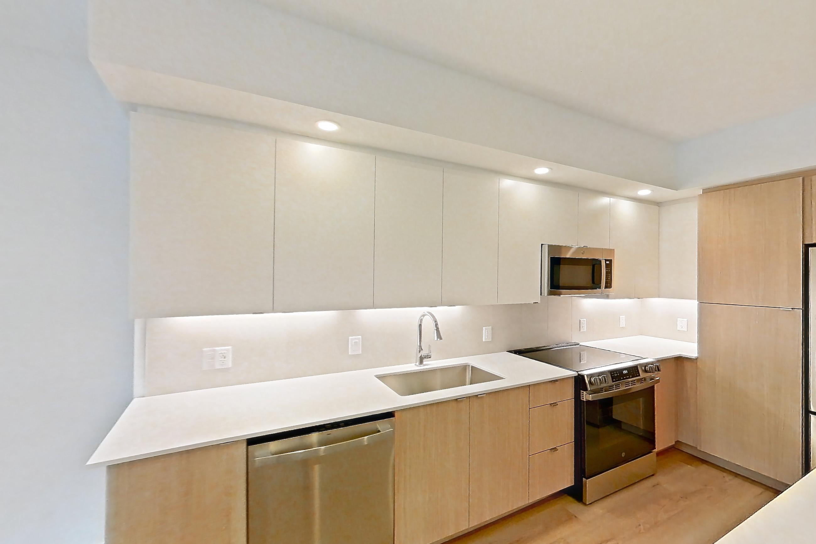 Kitchen island corner with dishwasher, light stone countertops, light wood-finish flooring, and stainless steel appliances, Apartment 101 at Caroline Pompano Beach