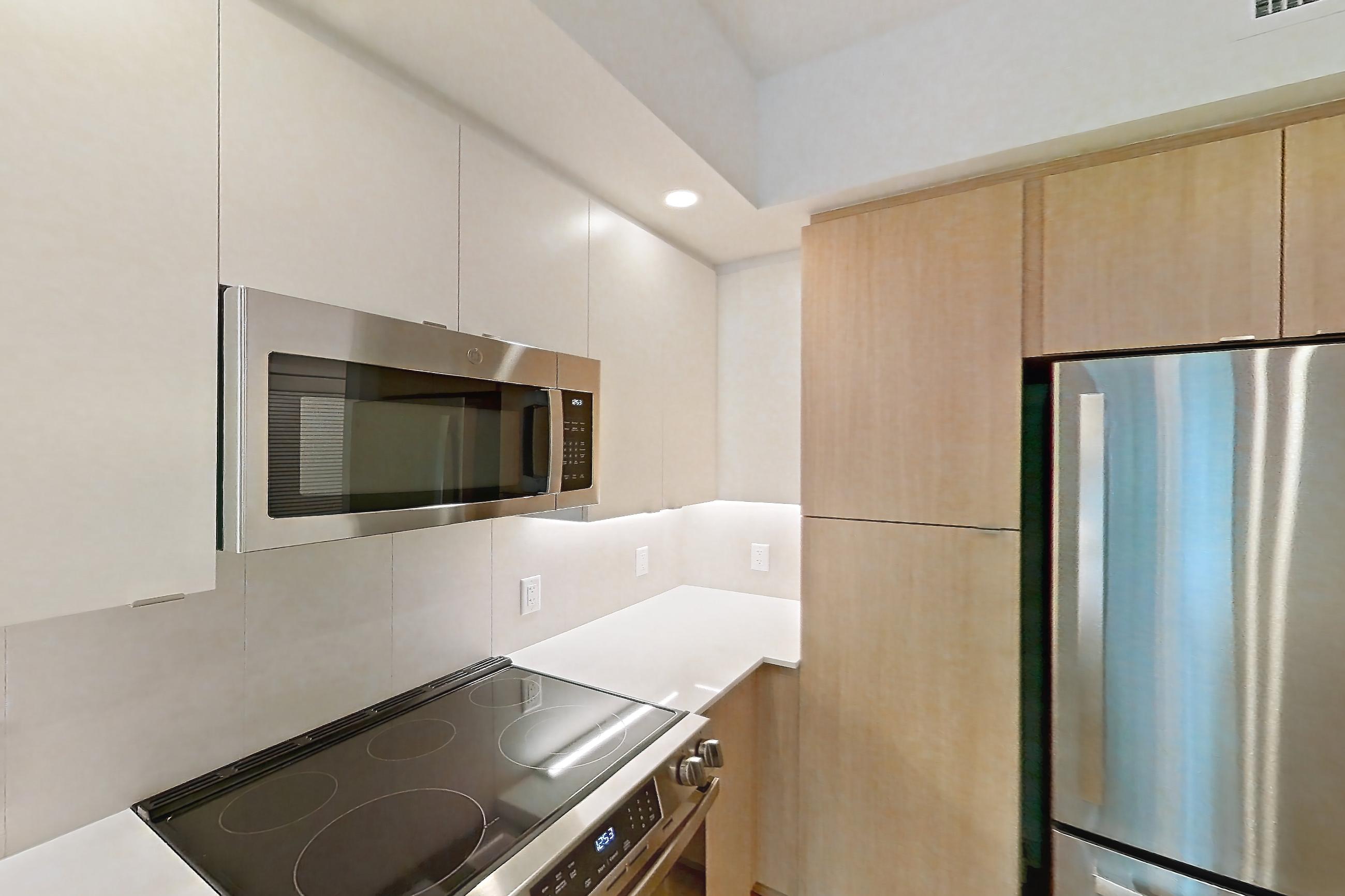 Kitchen with dishwasher, electric range, light countertops, light stone countertops, light wood-finish flooring, microwave, oven/range, refrigerator, and stainless steel appliances, Apartment 101 at Caroline Pompano Beach