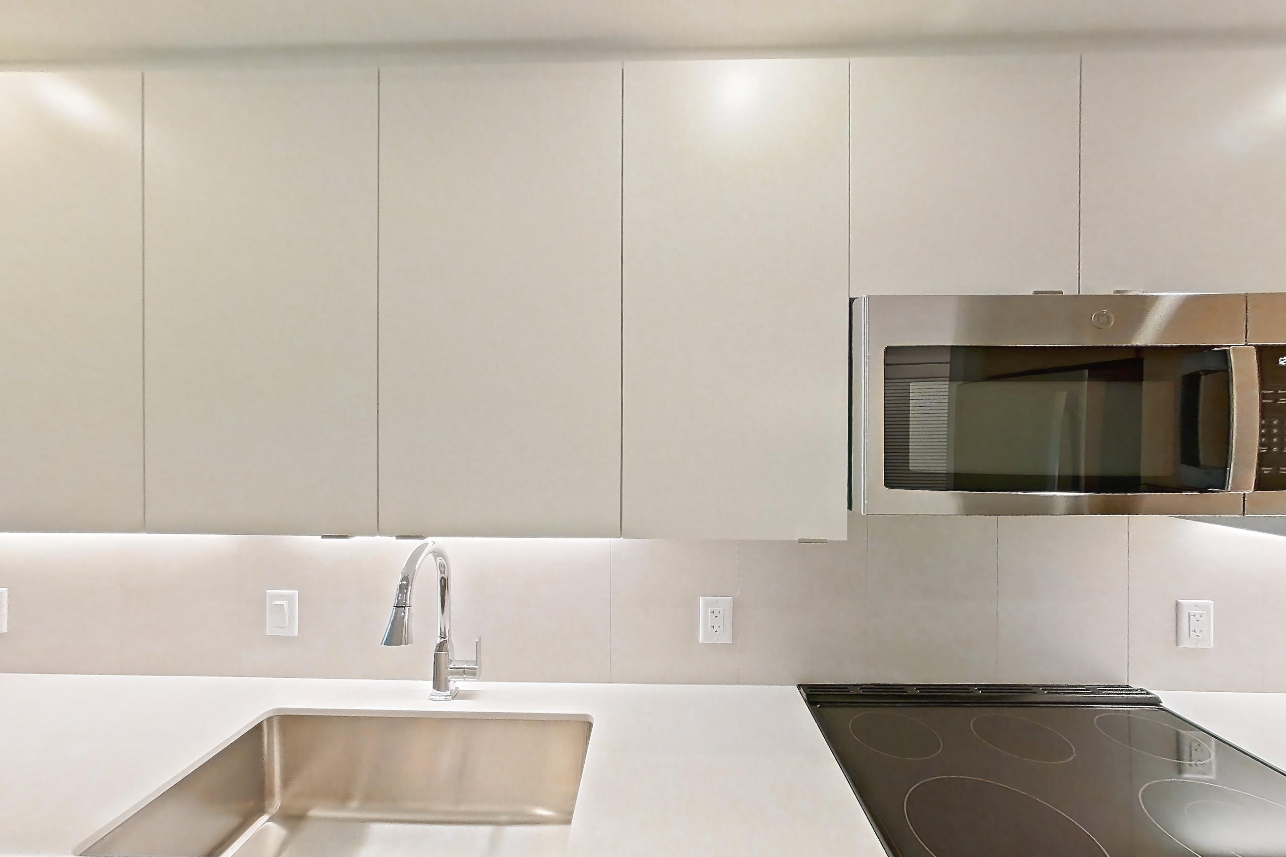 Kitchen with dishwasher, electric range, light countertops, light stone countertops, light wood-finish flooring, microwave, oven/range, refrigerator, and stainless steel appliances, Apartment 101 at Caroline Pompano Beach
