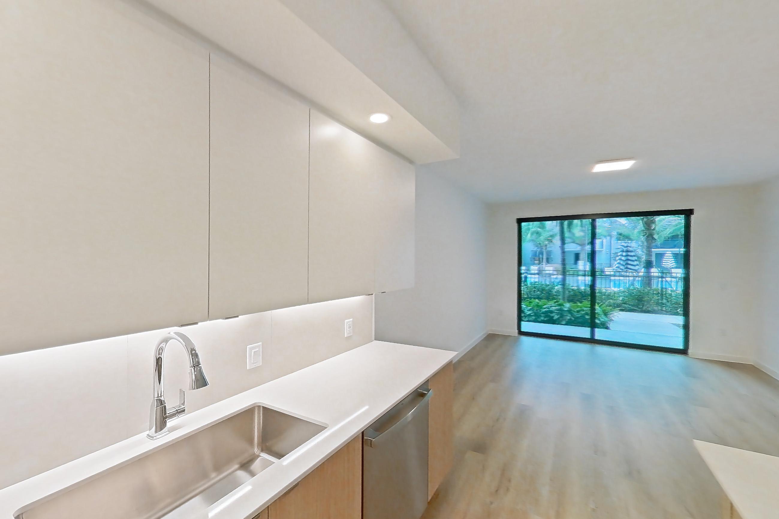Kitchen with dishwasher, electric range, light countertops, light wood-finish flooring, microwave, oven/range, refrigerator, and stainless steel appliances, Apartment 102 at Caroline Pompano Beach