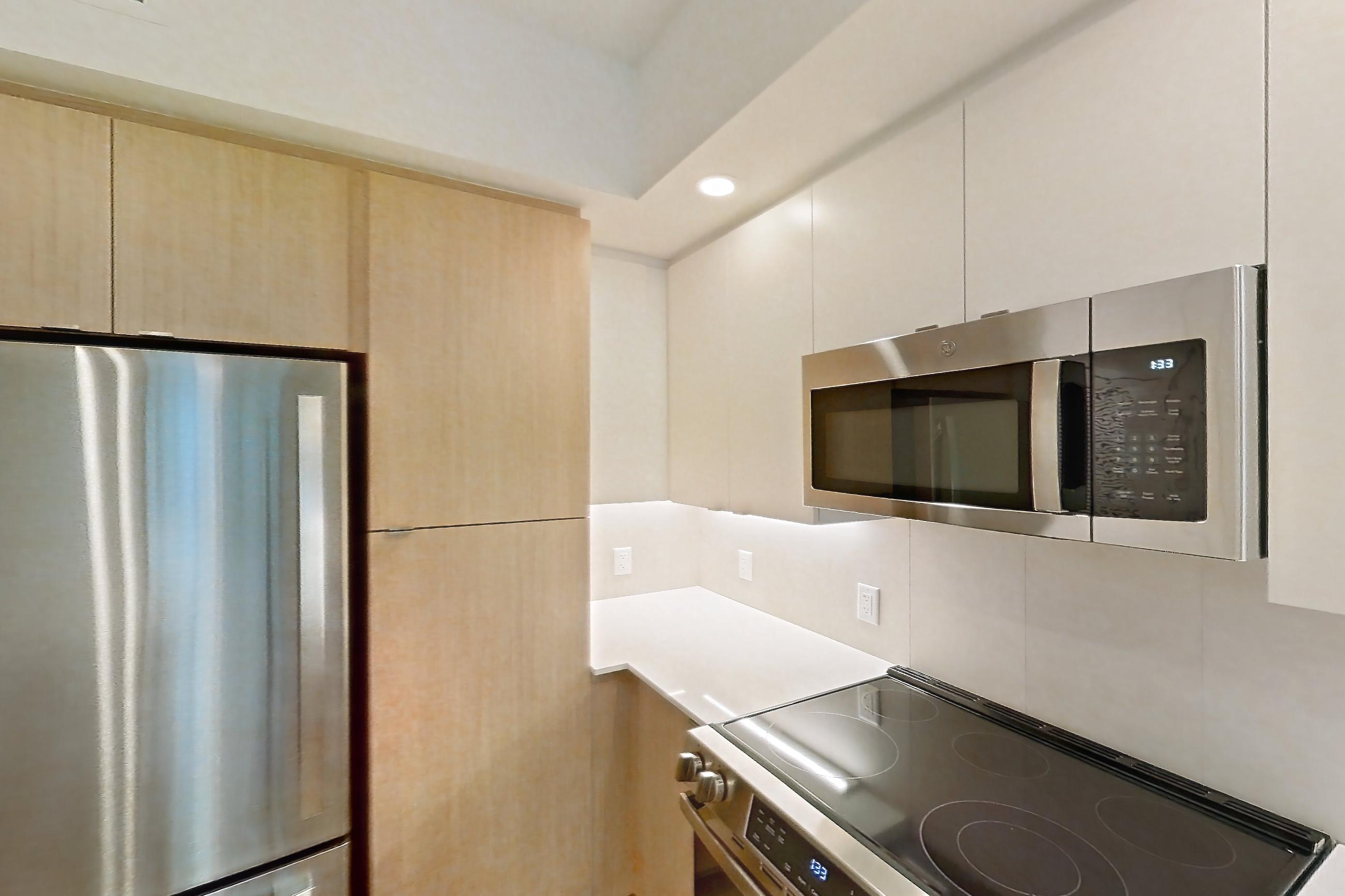 Kitchen with dishwasher, electric range, light countertops, light wood-finish flooring, microwave, oven/range, refrigerator, and stainless steel appliances, Apartment 102 at Caroline Pompano Beach