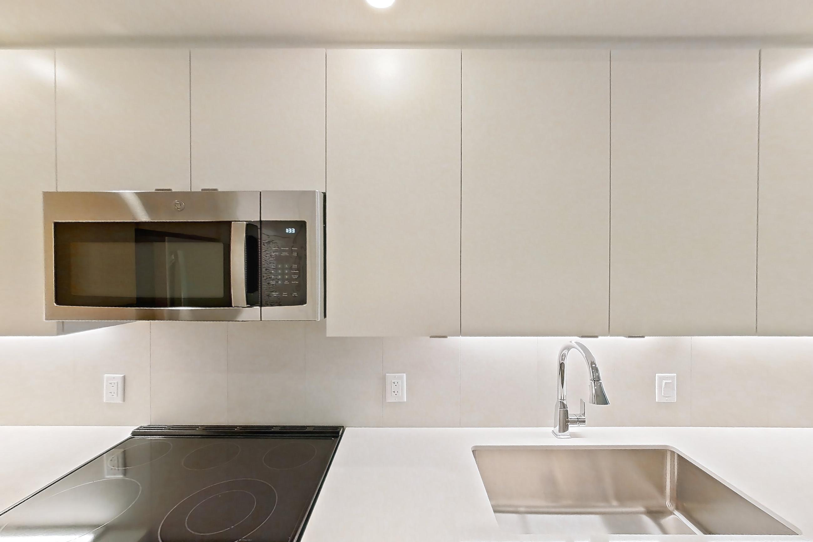 Kitchen with dishwasher, electric range, light countertops, light wood-finish flooring, microwave, oven/range, refrigerator, and stainless steel appliances, Apartment 102 at Caroline Pompano Beach