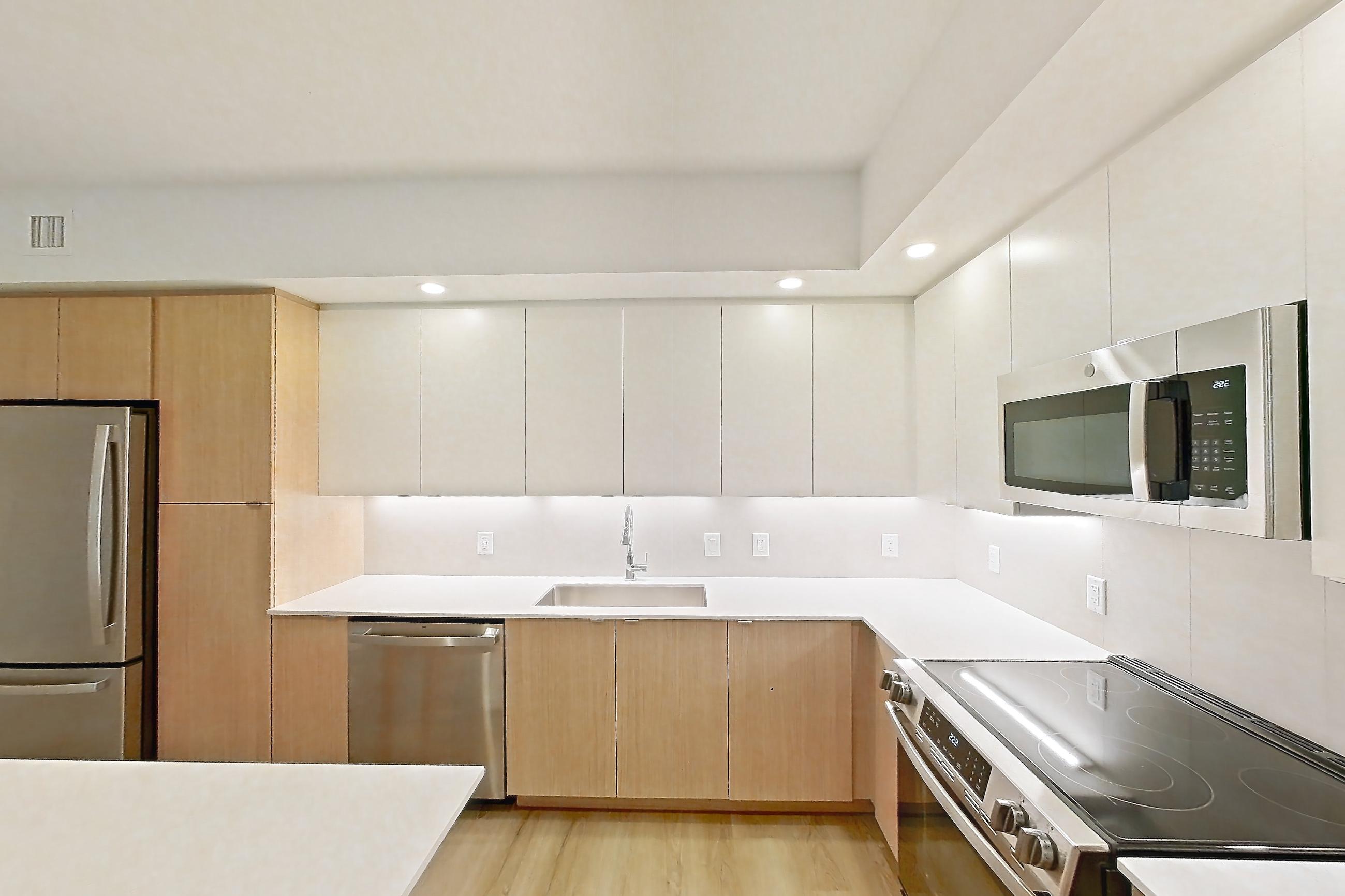 Kitchen island corner with electric range, light countertops, light wood-finish flooring, refrigerator, and stainless steel appliances, Apartment 103 at Caroline Pompano Beach