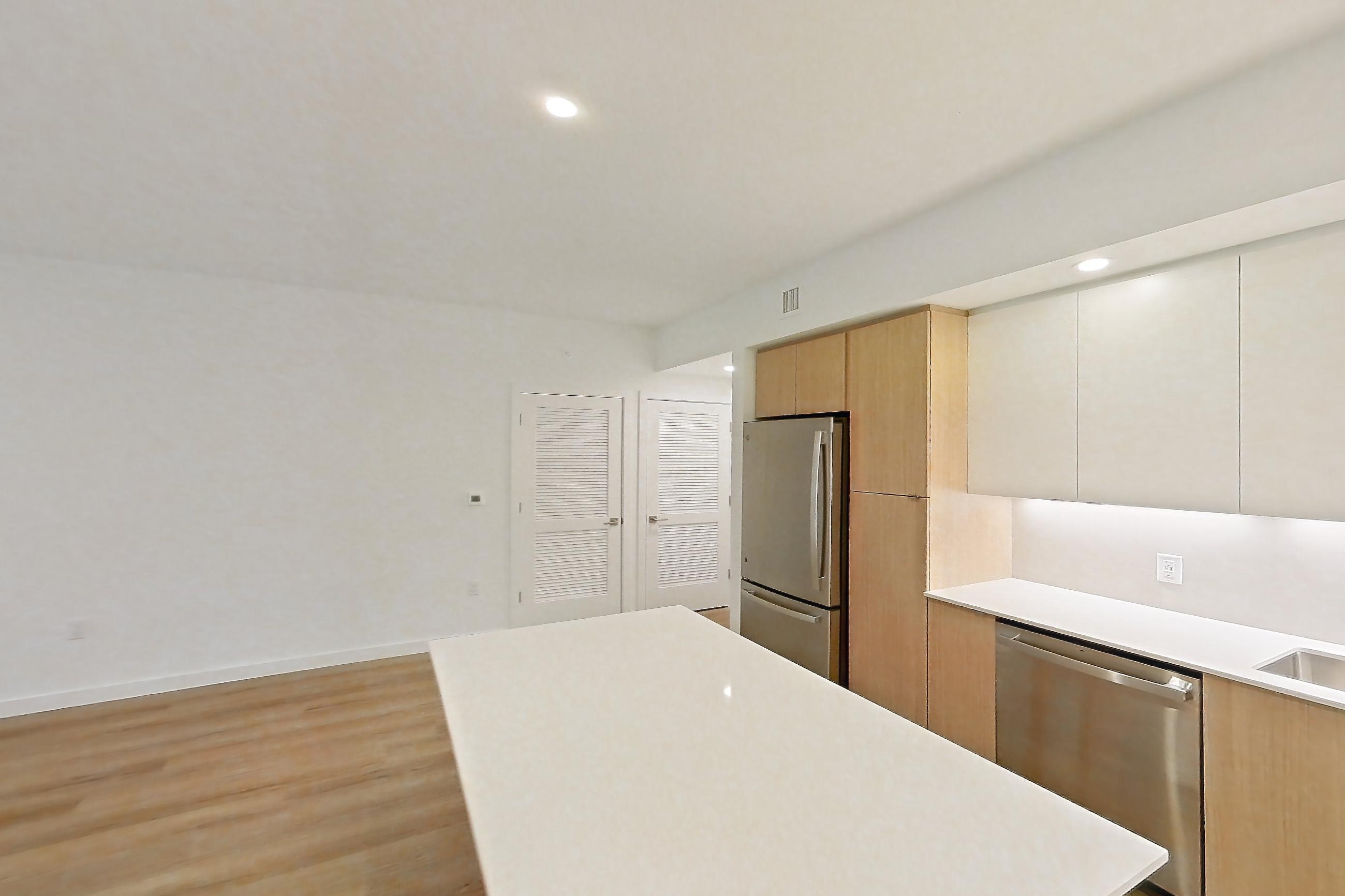 Kitchen island corner with electric range, light countertops, light wood-finish flooring, refrigerator, and stainless steel appliances, Apartment 103 at Caroline Pompano Beach