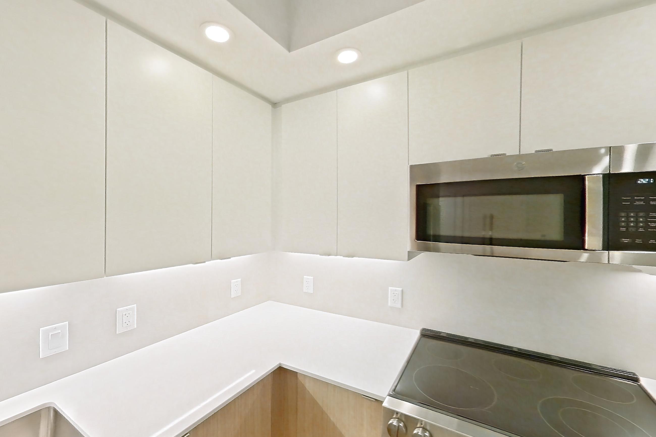 Kitchen with dishwasher, electric range, light countertops, light stone countertops, light wood-finish flooring, microwave, oven/range, refrigerator, and stainless steel appliances, Apartment 103 at Caroline Pompano Beach