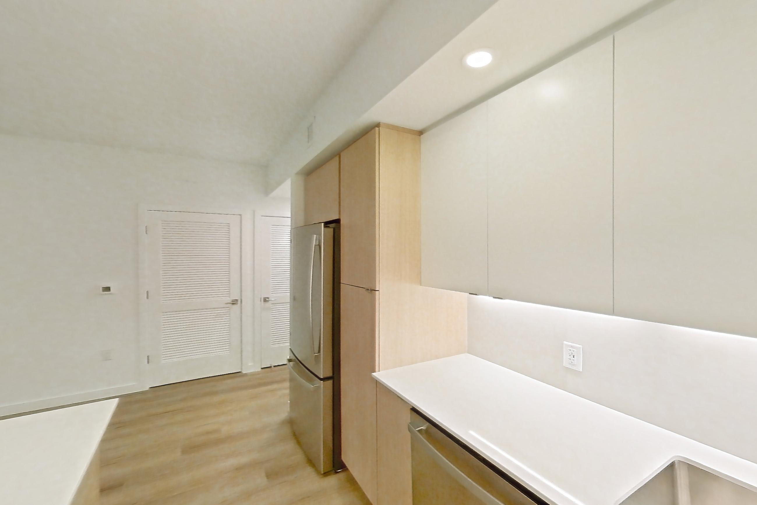 Kitchen with dishwasher, electric range, light countertops, light stone countertops, light wood-finish flooring, microwave, oven/range, refrigerator, and stainless steel appliances, Apartment 103 at Caroline Pompano Beach