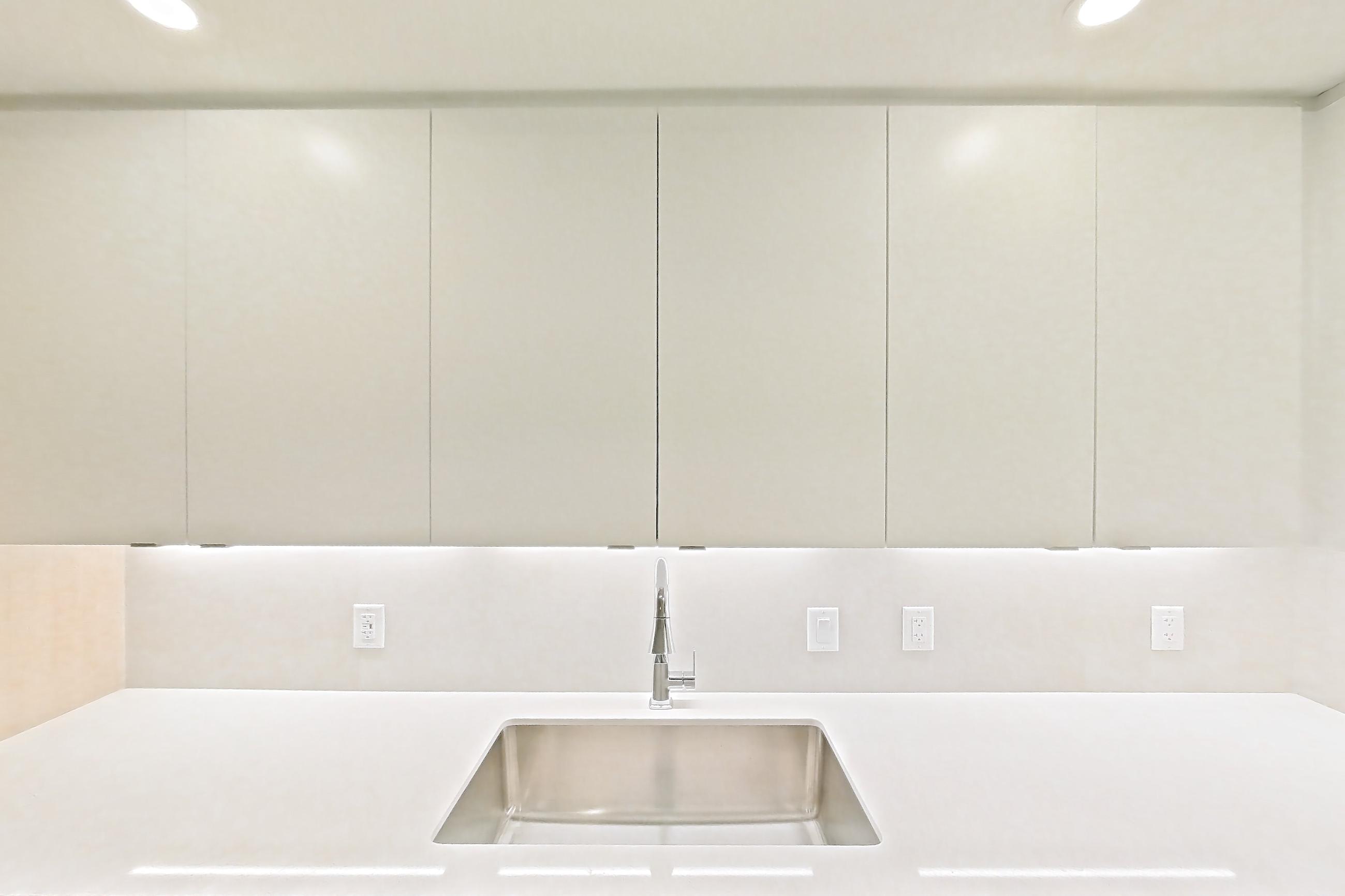 Kitchen with dishwasher, electric range, light countertops, light stone countertops, light wood-finish flooring, microwave, oven/range, refrigerator, and stainless steel appliances, Apartment 103 at Caroline Pompano Beach