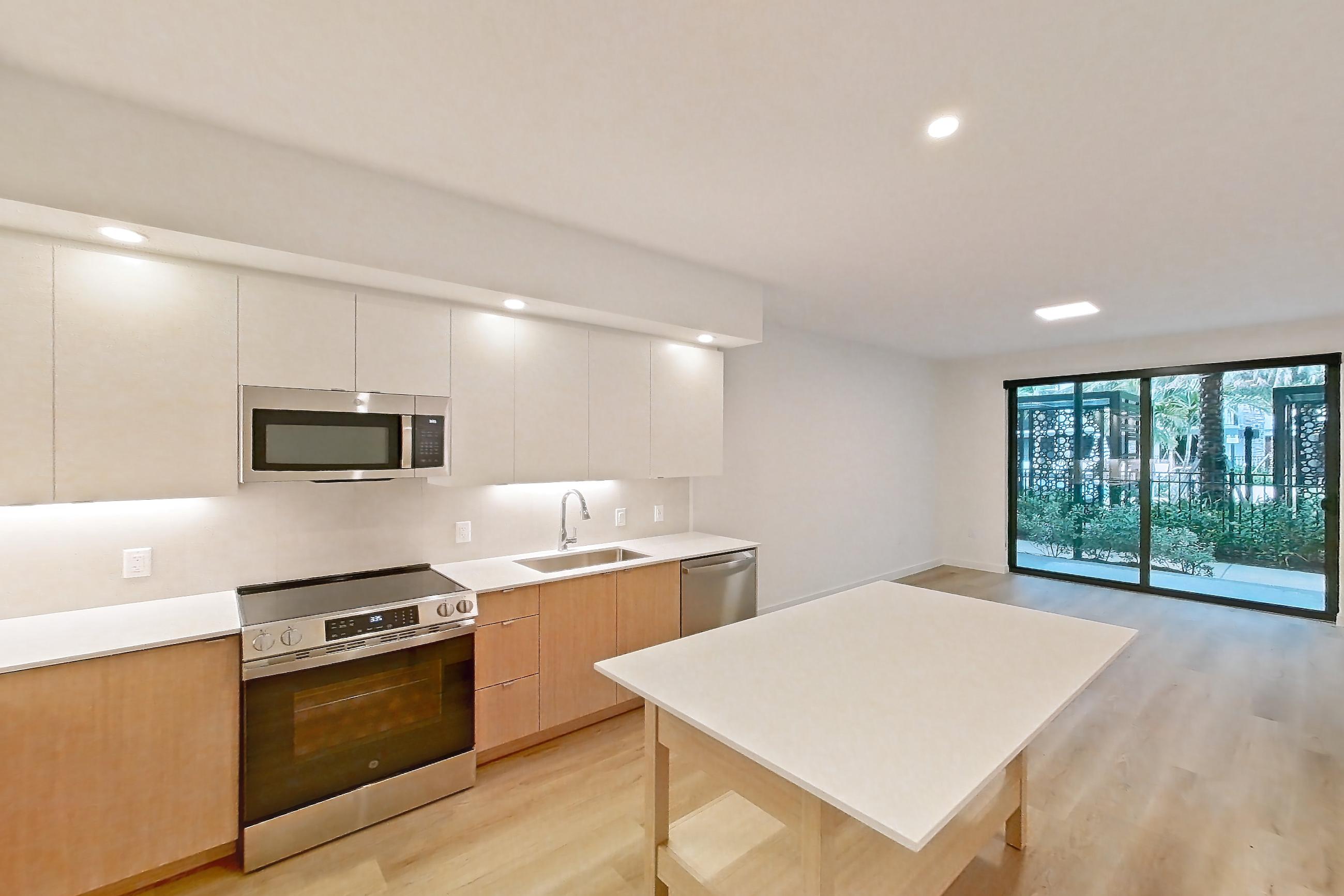 Kitchen entryway with dishwasher, electric range, light countertops, light wood-finish flooring, oven/range, refrigerator, and stainless steel appliances, Apartment 104 at Caroline Pompano Beach