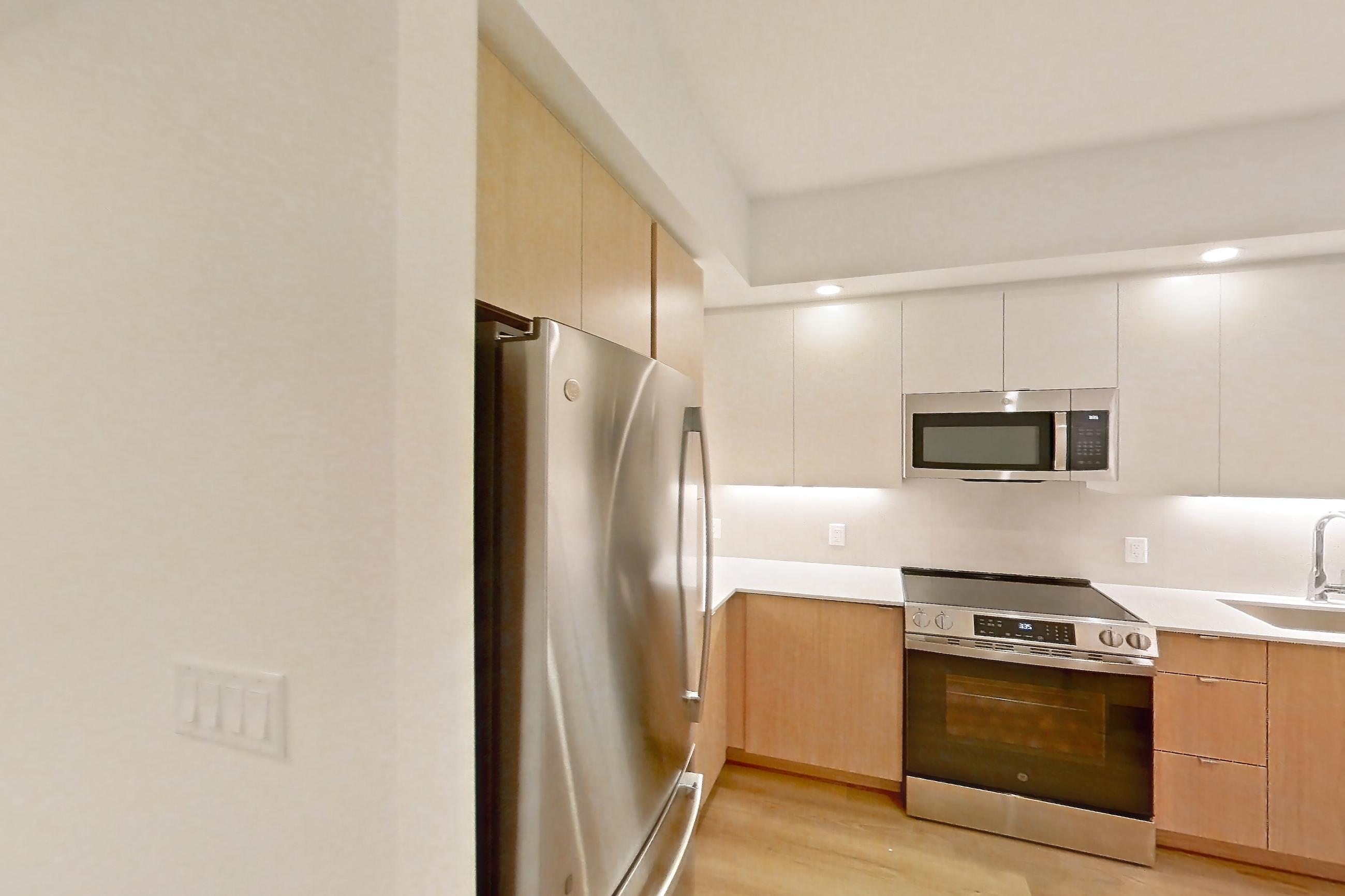 Kitchen entryway with dishwasher, electric range, light countertops, light wood-finish flooring, oven/range, refrigerator, and stainless steel appliances, Apartment 104 at Caroline Pompano Beach