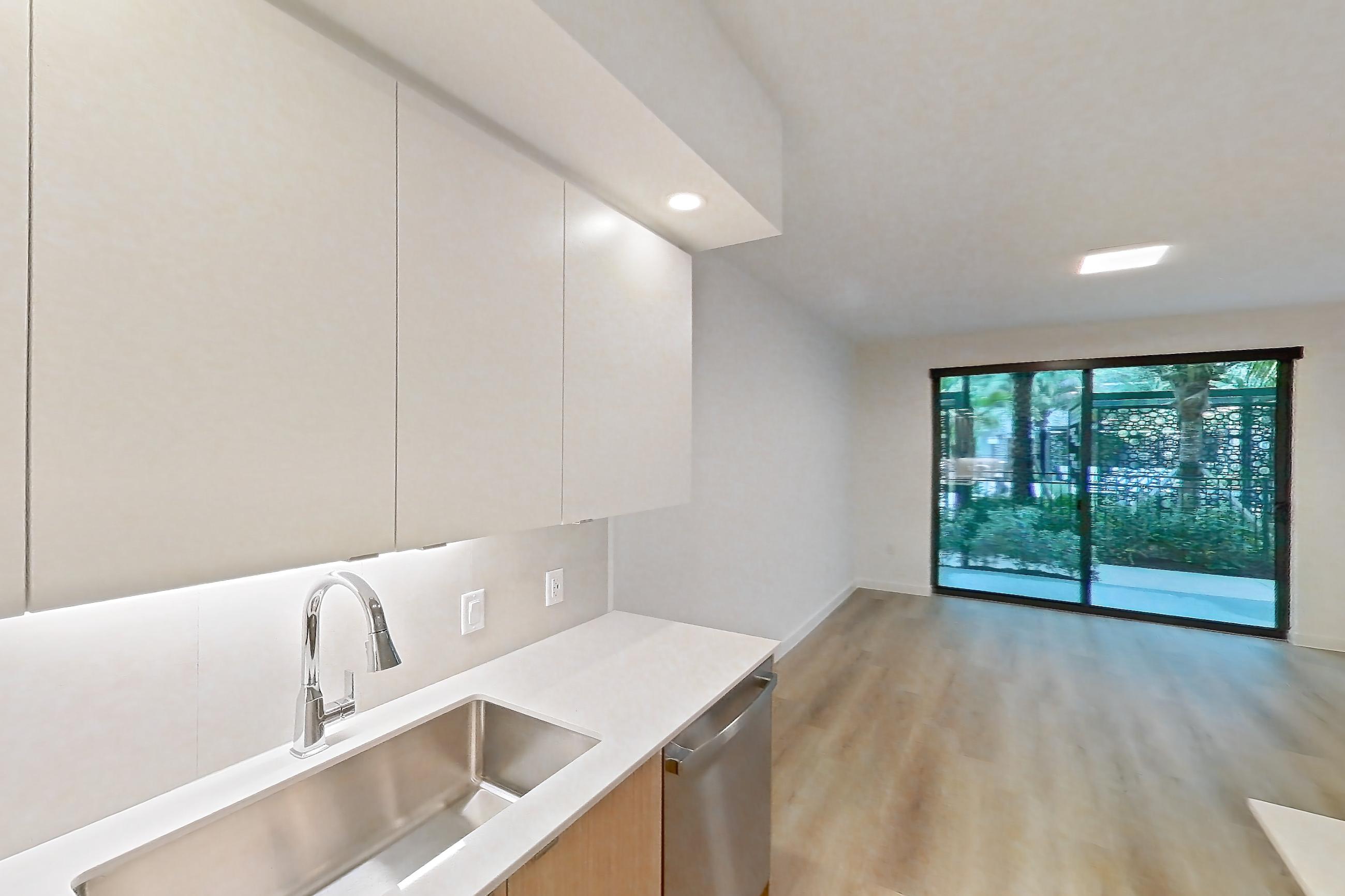 Kitchen with dishwasher, electric range, light countertops, light stone countertops, light wood-finish flooring, microwave, oven/range, refrigerator, and stainless steel appliances, Apartment 104 at Caroline Pompano Beach