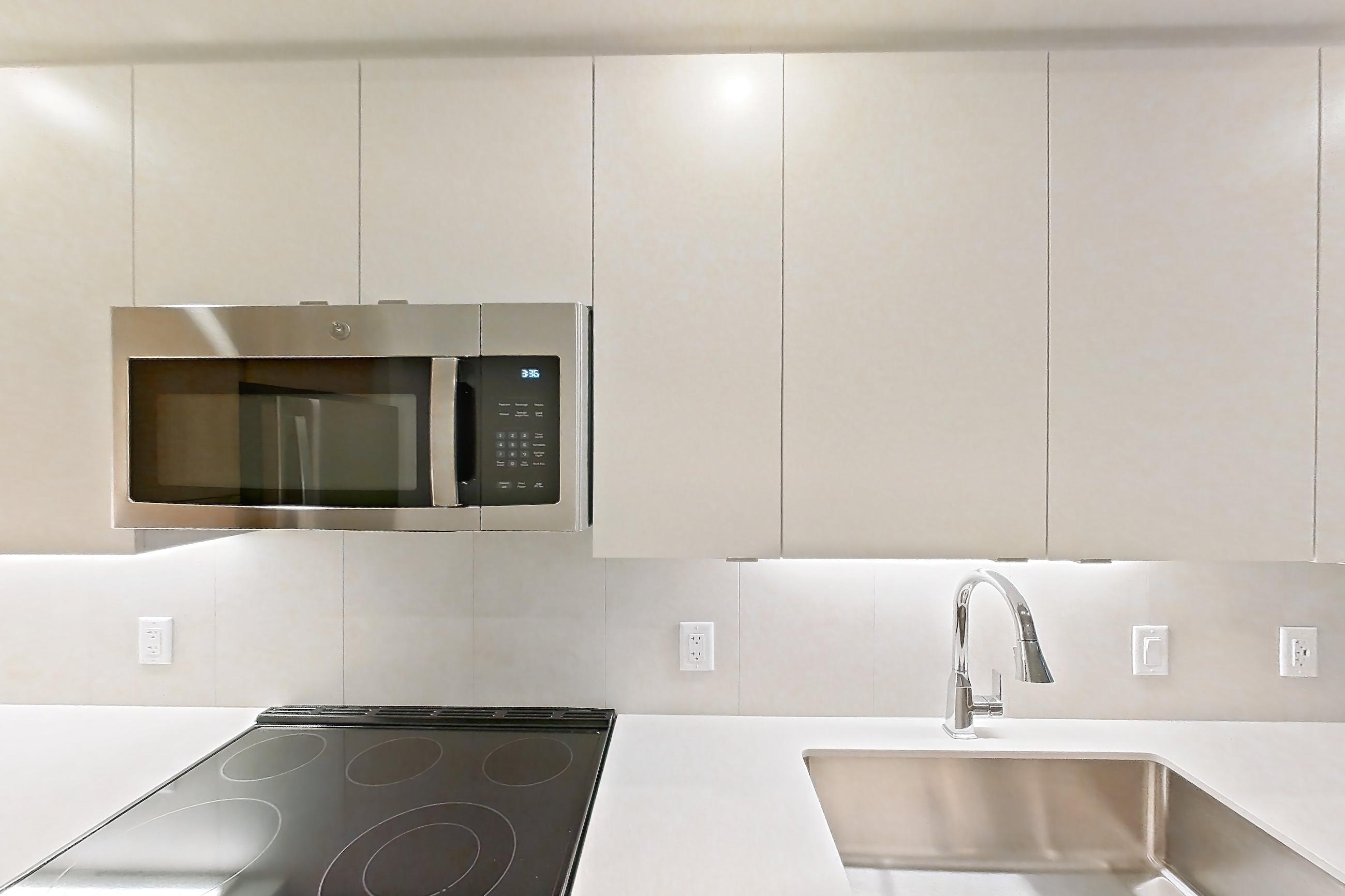 Kitchen with dishwasher, electric range, light countertops, light stone countertops, light wood-finish flooring, microwave, oven/range, refrigerator, and stainless steel appliances, Apartment 104 at Caroline Pompano Beach
