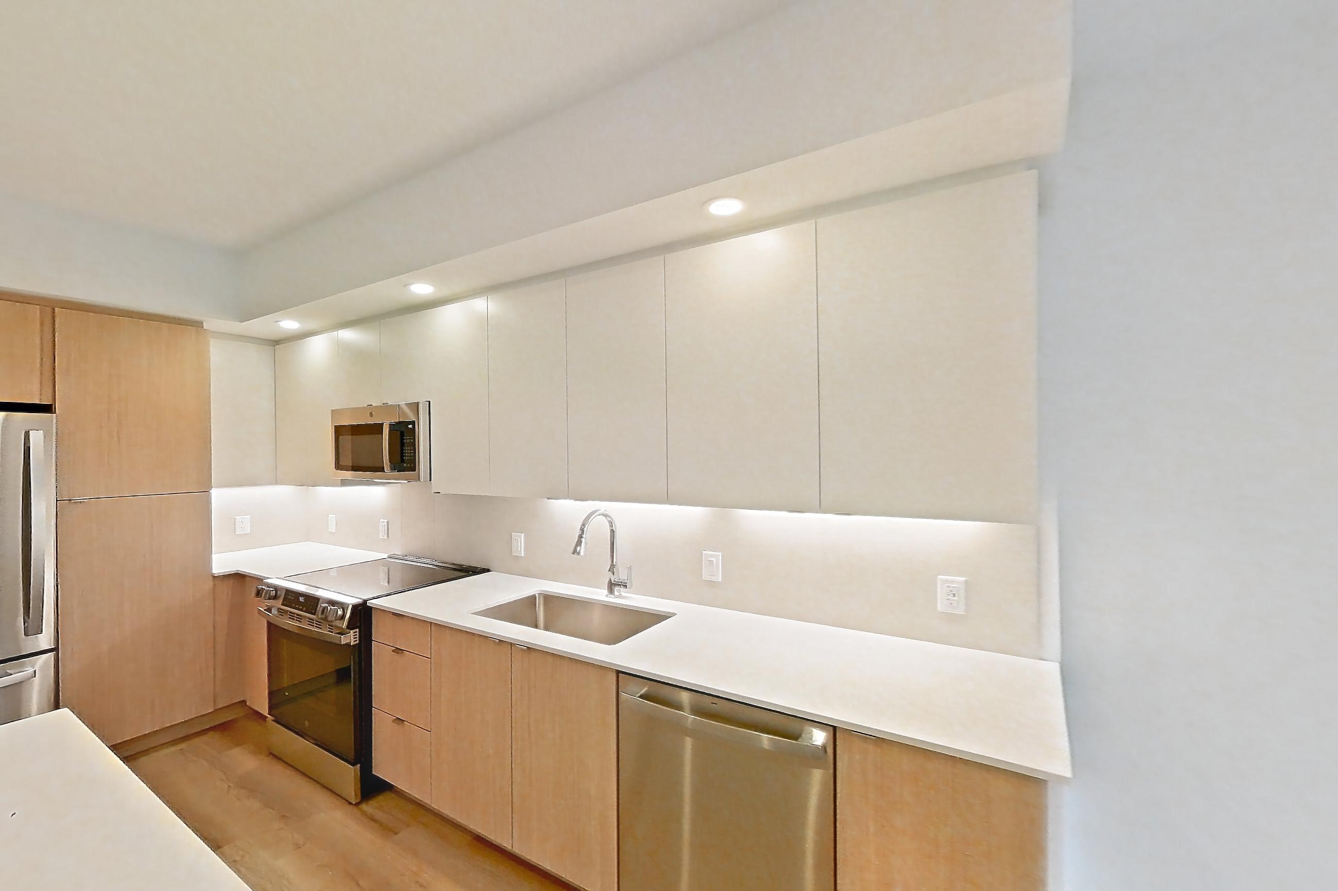 Kitchen island corner with dishwasher, light countertops, light wood-finish flooring, and stainless steel appliances, Apartment 105 at Caroline Pompano Beach