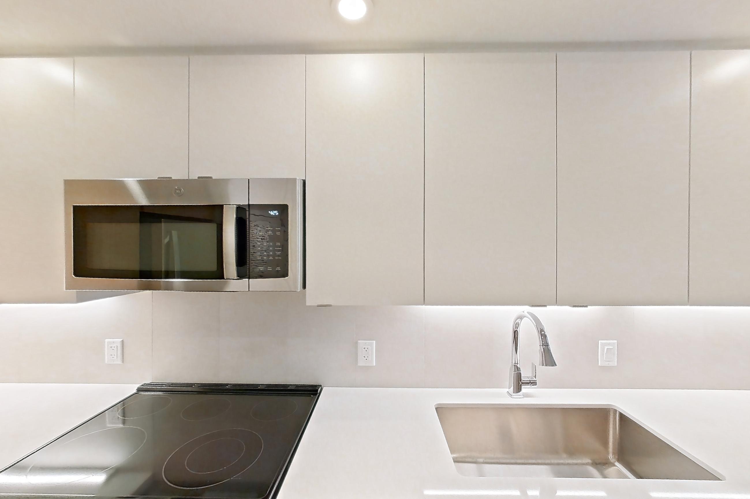 Kitchen with dishwasher, electric range, light countertops, light stone countertops, light wood-finish flooring, microwave, oven/range, refrigerator, and stainless steel appliances, Apartment 105 at Caroline Pompano Beach