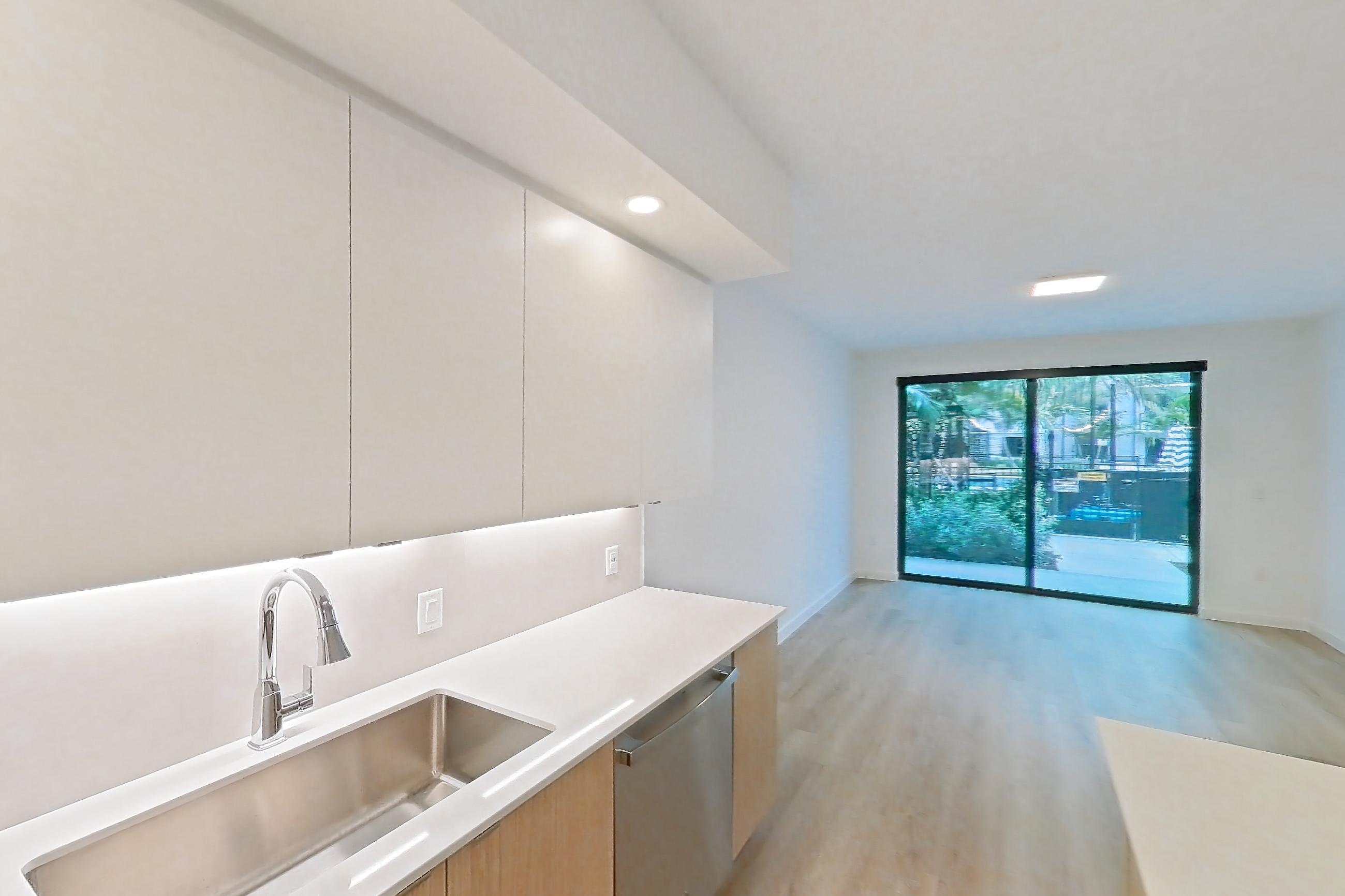 Kitchen with dishwasher, electric range, light countertops, light stone countertops, light wood-finish flooring, microwave, oven/range, refrigerator, and stainless steel appliances, Apartment 105 at Caroline Pompano Beach