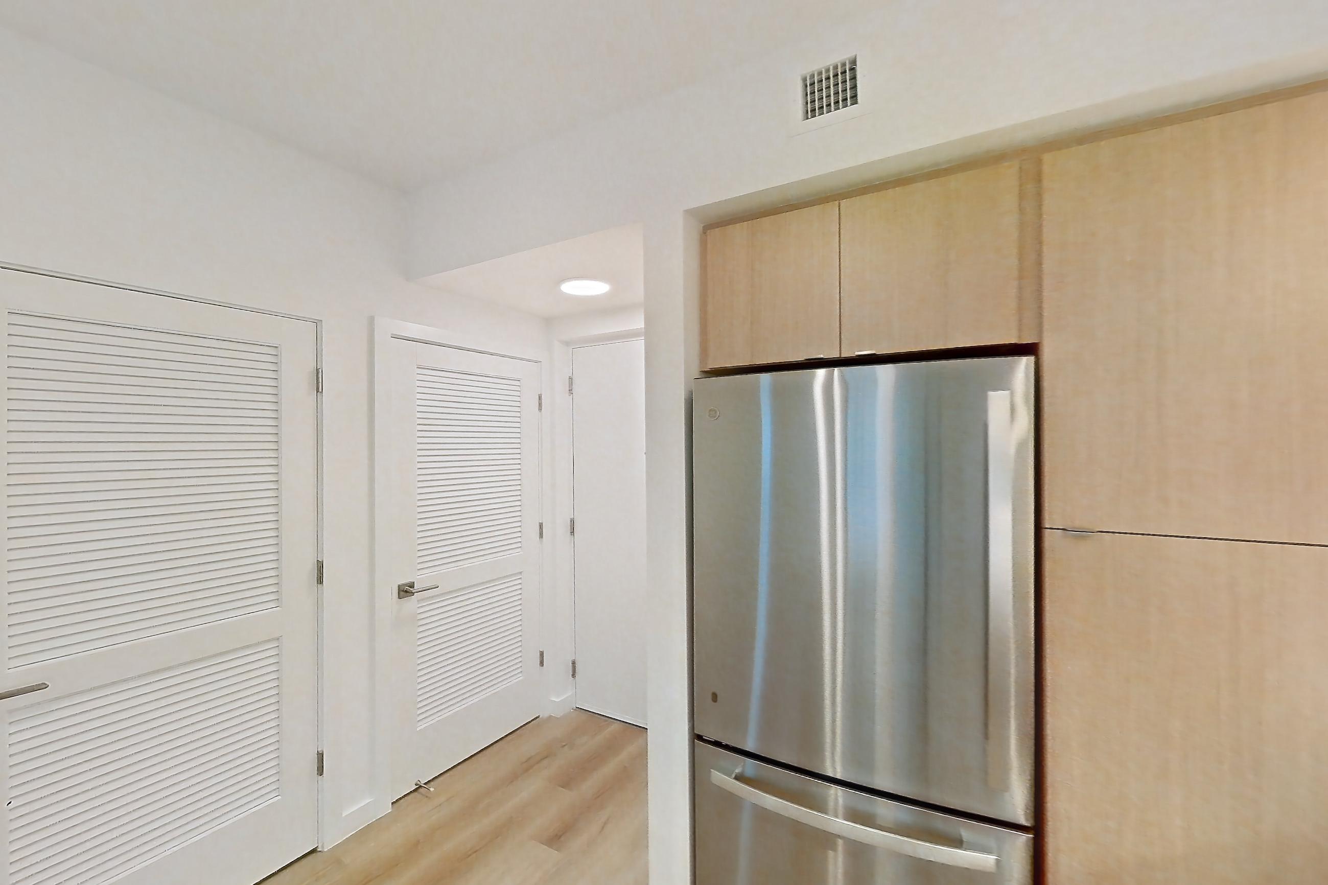 Kitchen with dishwasher, electric range, light countertops, light stone countertops, light wood-finish flooring, microwave, oven/range, refrigerator, and stainless steel appliances, Apartment 105 at Caroline Pompano Beach