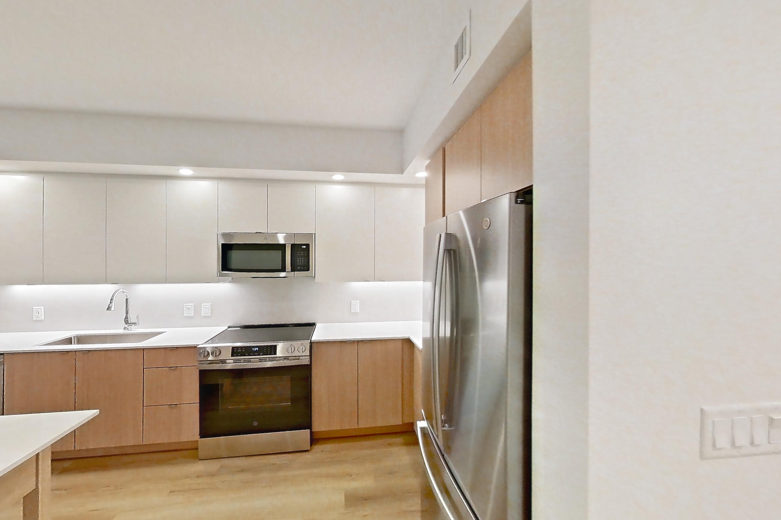 Kitchen entryway with dishwasher, electric range, light countertops, light wood-finish flooring, oven/range, refrigerator, and stainless steel appliances, Apartment 106 at Caroline Pompano Beach