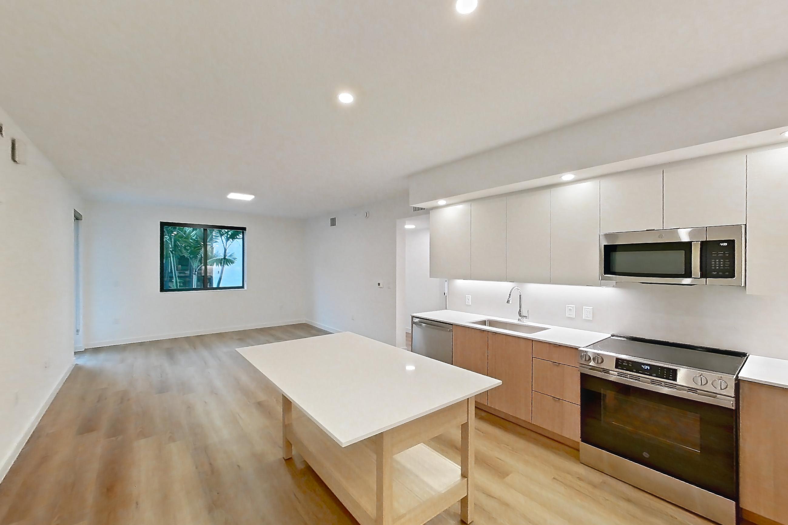 Kitchen entryway with dishwasher, electric range, light countertops, light wood-finish flooring, oven/range, refrigerator, and stainless steel appliances, Apartment 106 at Caroline Pompano Beach