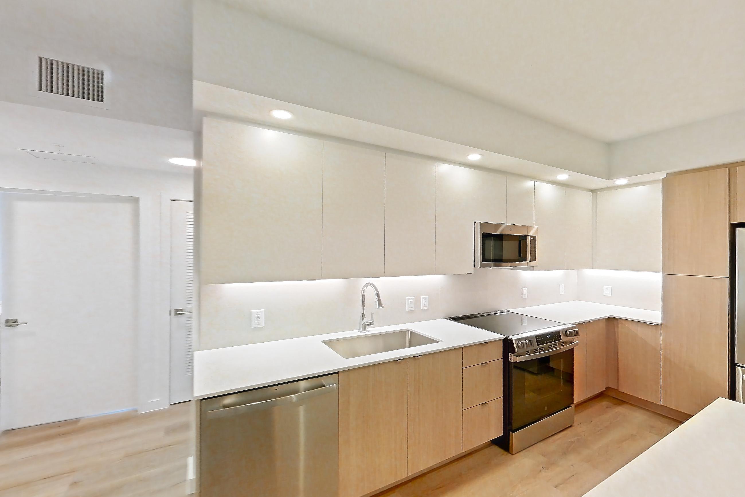 Kitchen island corner with dishwasher, light stone countertops, light wood-finish flooring, and stainless steel appliances, Apartment 106 at Caroline Pompano Beach