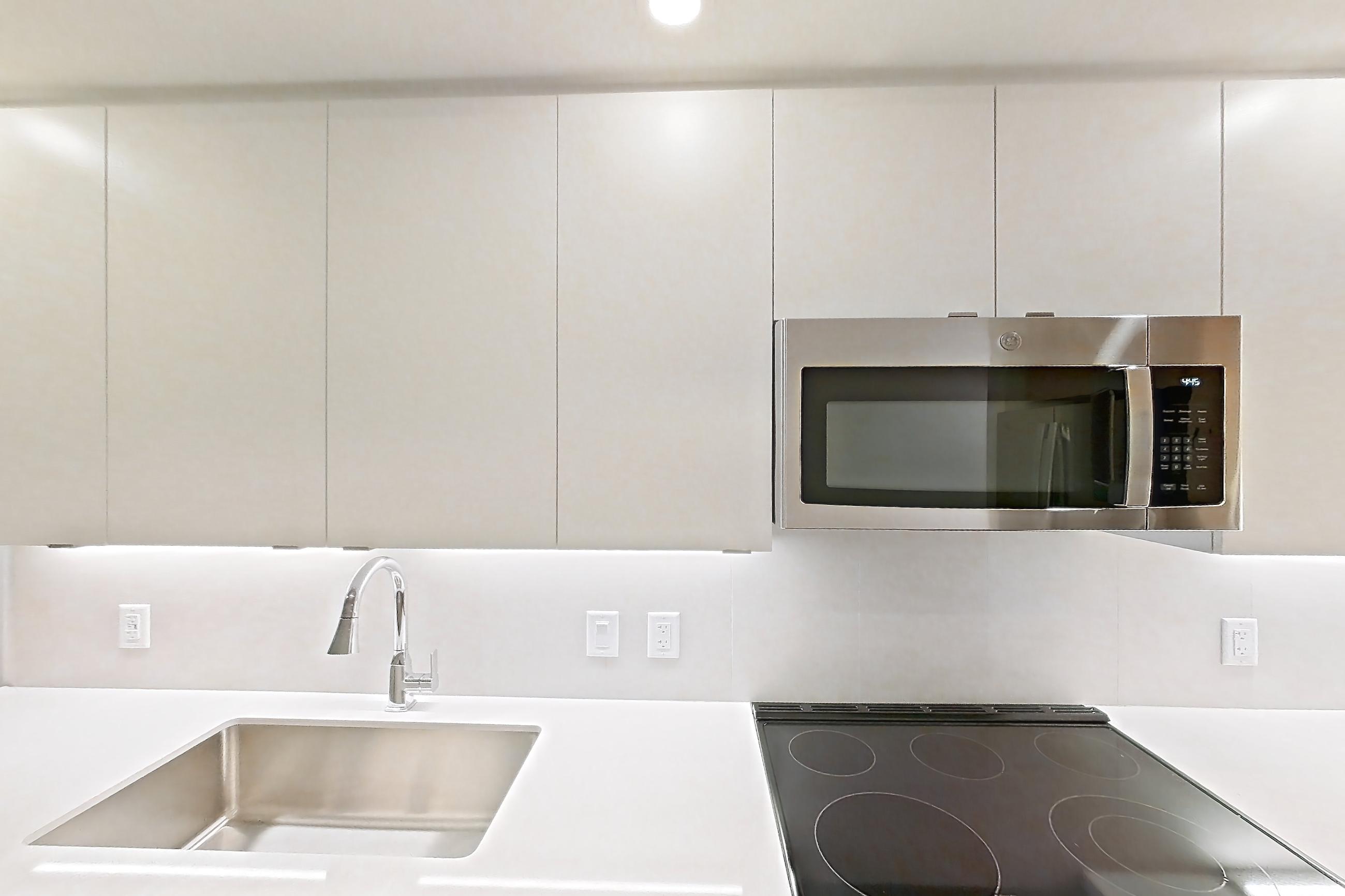 Kitchen with dishwasher, electric range, light countertops, light stone countertops, light wood-finish flooring, microwave, oven/range, refrigerator, and stainless steel appliances, Apartment 106 at Caroline Pompano Beach