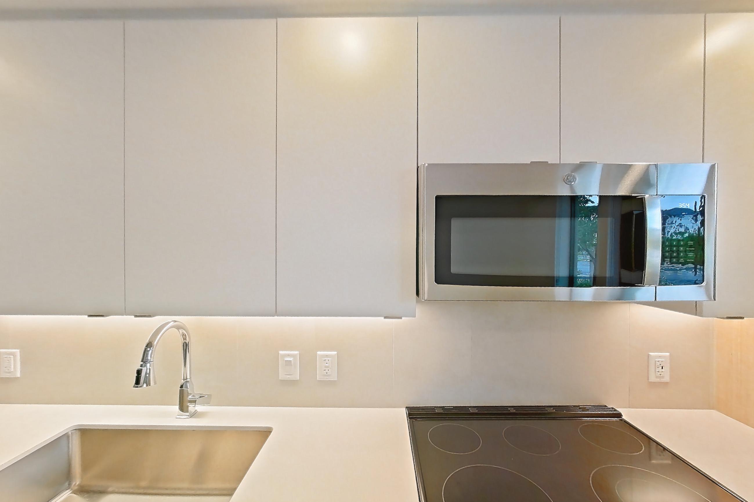 Kitchen with electric range, light countertops, light wood-finish flooring, microwave, oven/range, refrigerator, and stainless steel appliances, Apartment 109 at Caroline Pompano Beach